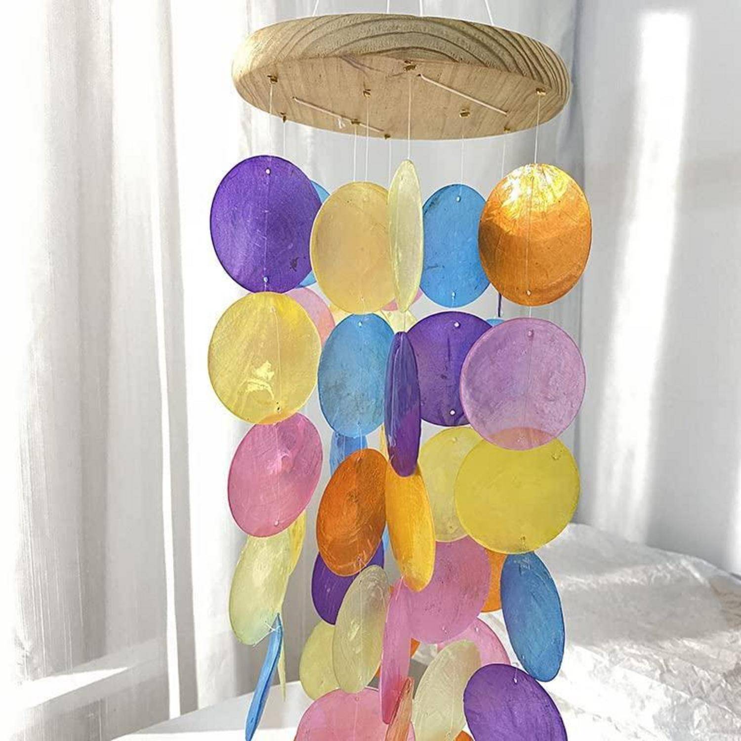 Buntes hängendes Mobile aus durchsichtigen ovalen Scheiben in Lila, Gelb, Blau, Rosa und Orange, die von einem Holzring aufgehängt sind.