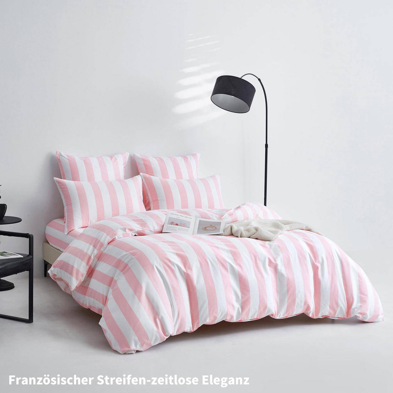 Rosa-weiß gestreiftes Bettwäsche auf einem ordentlich gemachten Bett mit einer schwarzen Stehlampe in einem minimalistischen weißen Schlafzimmer.