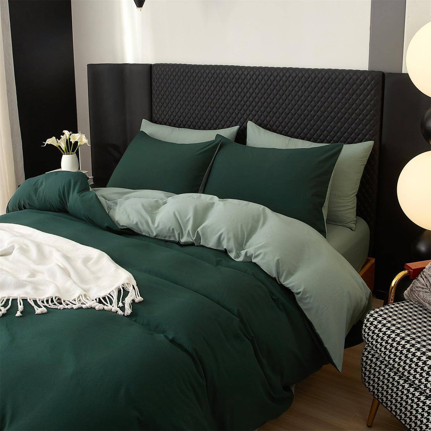 Ein ordentlich gemachtes Bett mit dunkelgrüner Bettwäsche, übereinander gestapelten Kissen, einem gesteppten schwarzen Kopfteil und einer weißen Wurfdecke in einem modernen Schlafzimmer.