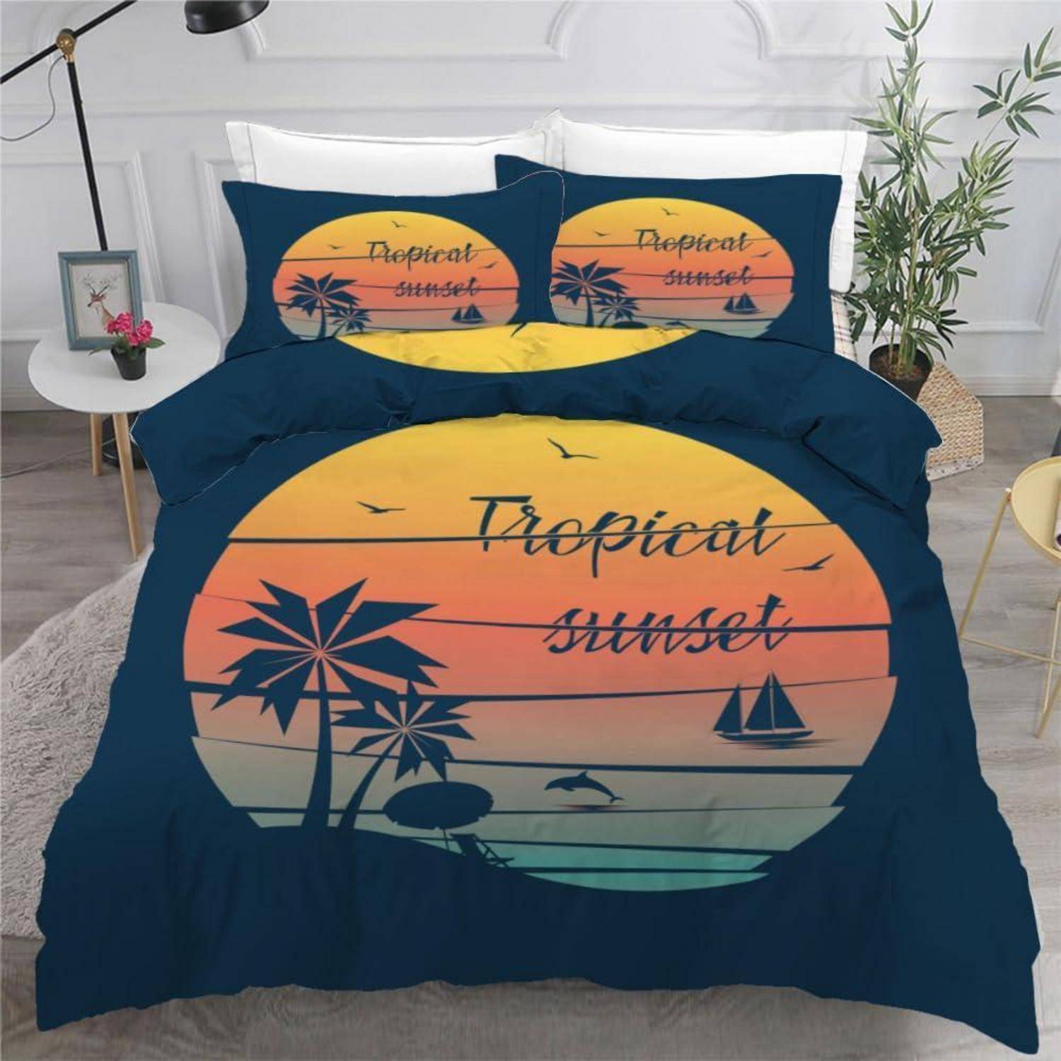 Bett mit dunkelblauem Bettwaren-Set, das eine große Grafik eines tropischen Sonnenuntergangs mit Palmen und einem Segelboot zeigt, plus passende Kissenbezüge.