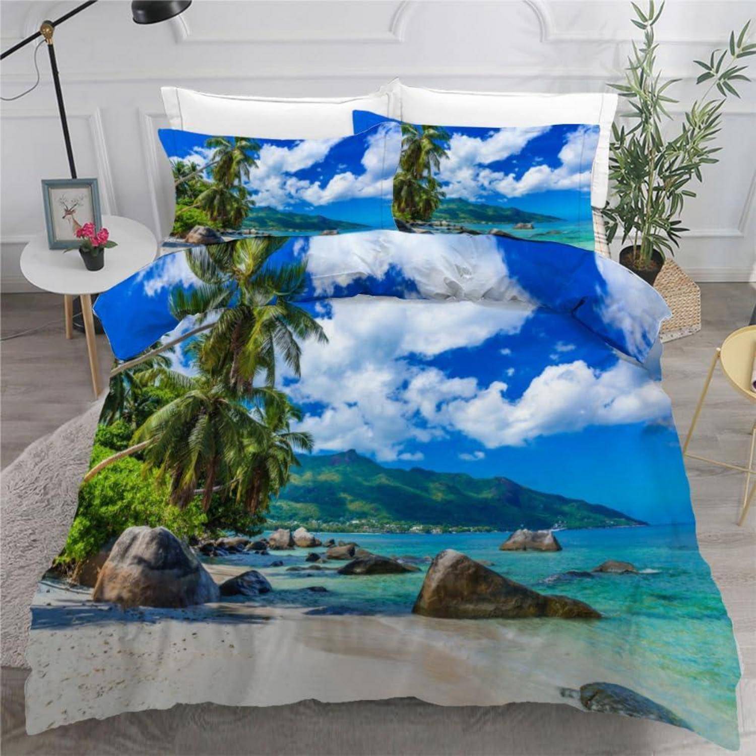Bett mit tropischem Strand-Bettwäsche-Druck mit Palmen, blauem Himmel, türkisblauem Wasser und felsiger Küstenlinie in einem hellen Schlafzimmer.