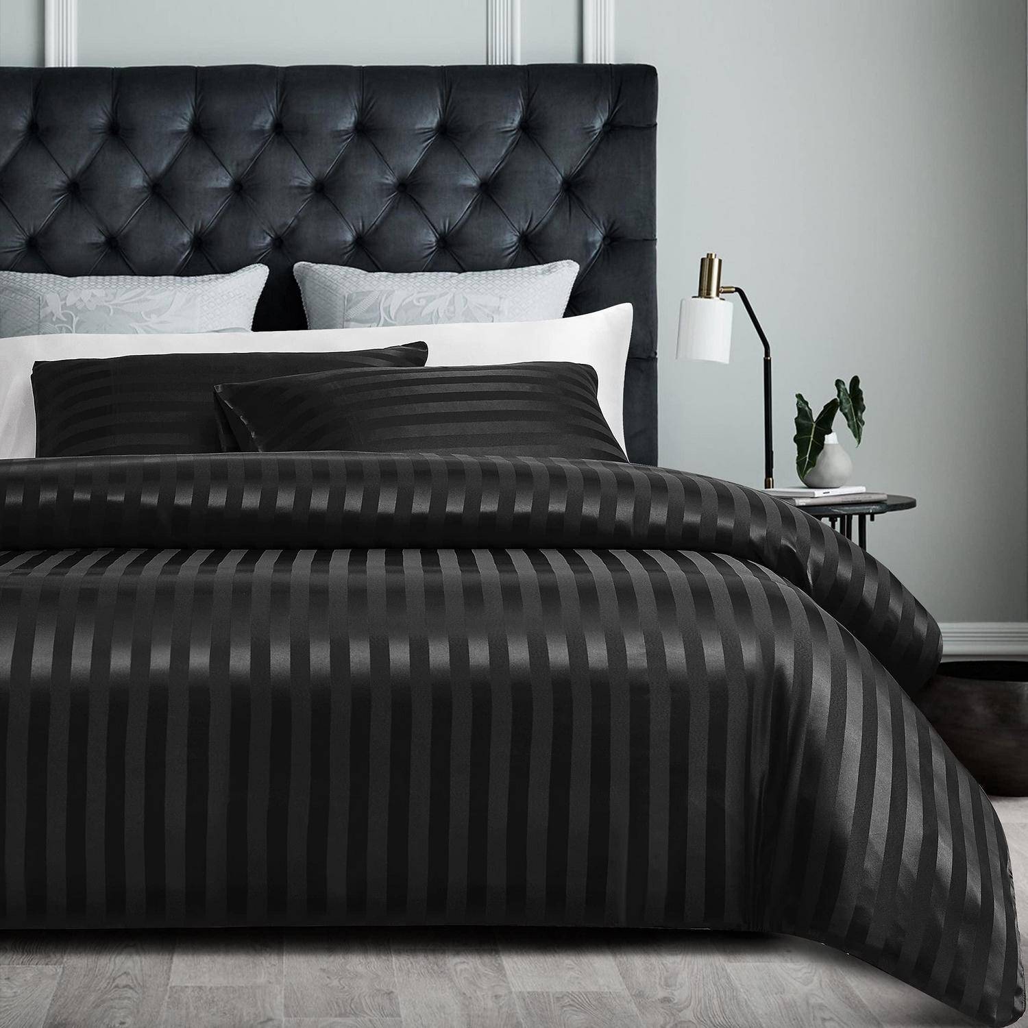 Schwarz gestreiftes Bettwäsche auf einem gemachten Bett mit gepolstertem schwarzem Kopfteil und Nachttischlampe in einem modernen grauem Schlafzimmer.