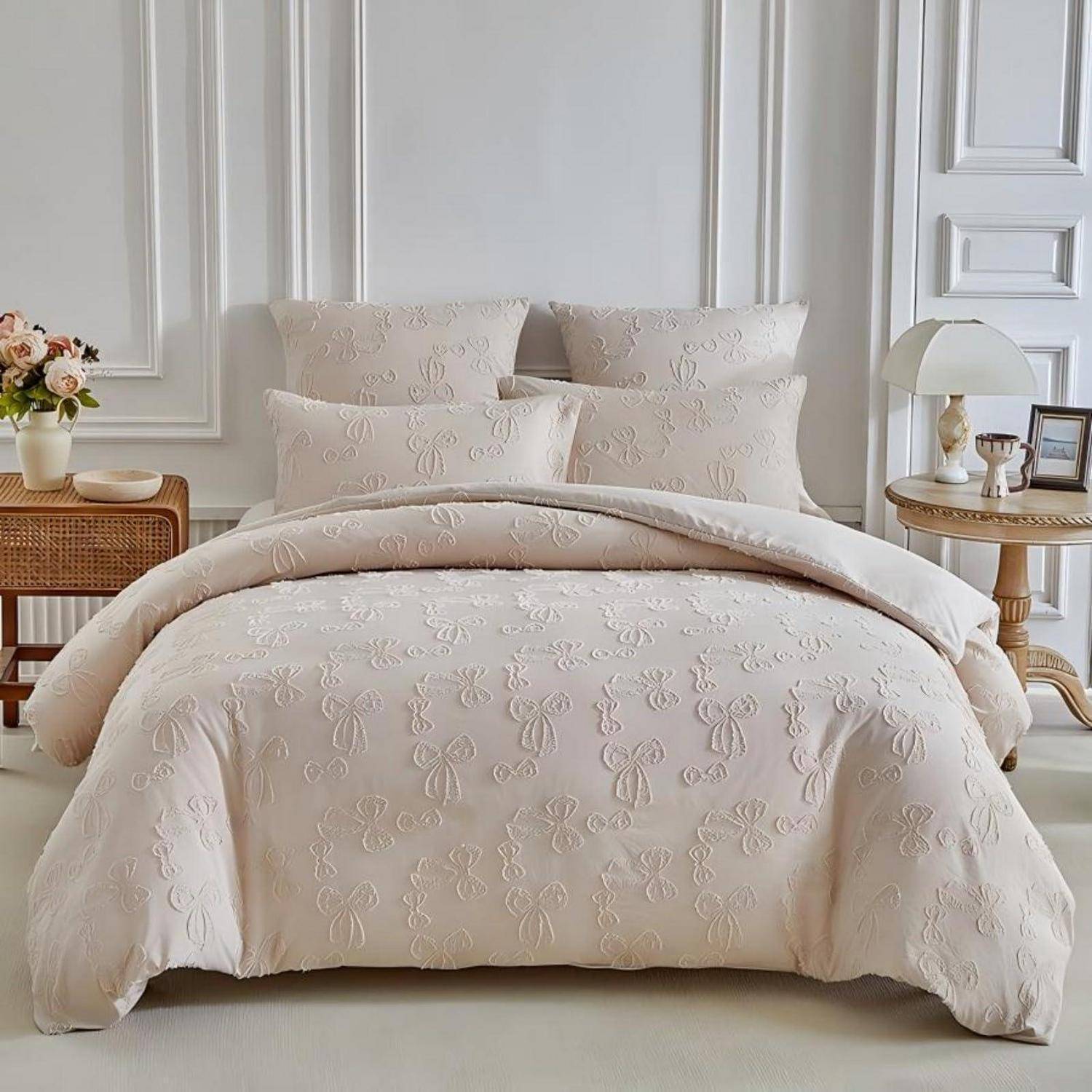 Ein ordentlich gemachtes Bett mit cremefarbener bestickter Bettwäsche und Kissen in einem hellen, eleganten Schlafzimmer mit Nachttischen und Lampen.