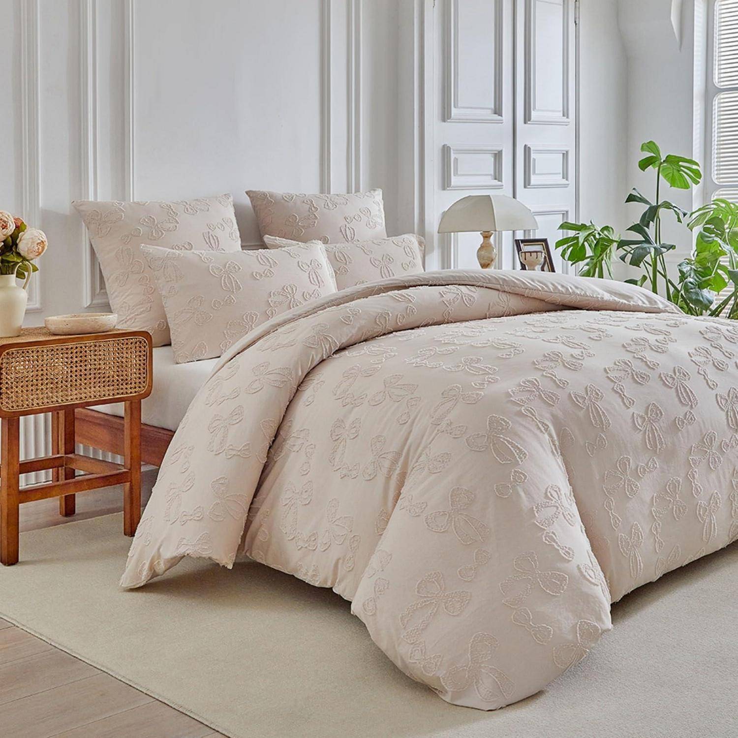 Ein ordentlich gemachtes Bett mit beigefarbener Blumenbettwäsche und Kissen in einem hellen Schlafzimmer, neben einem geflochtenen Nachttisch, einer Pflanze und einem Fenster.