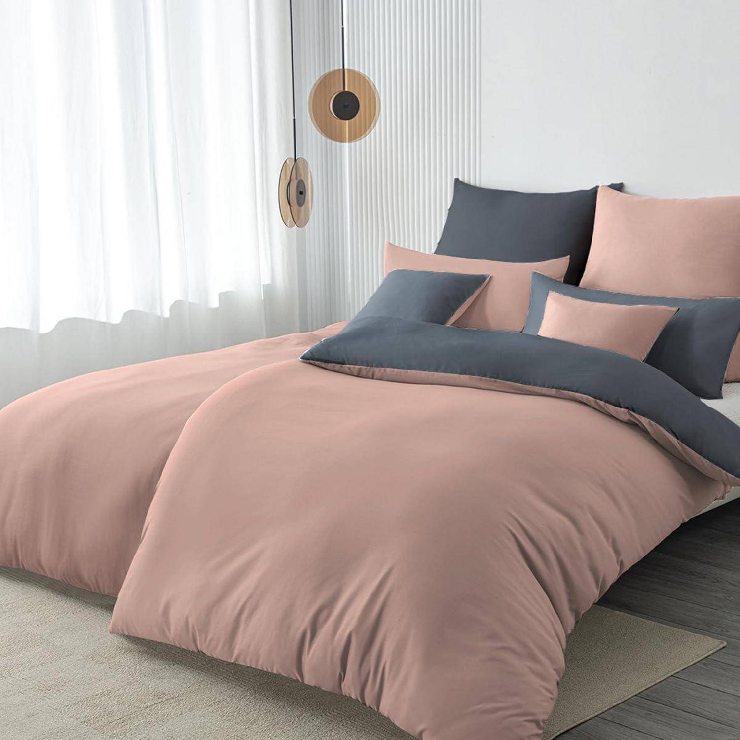 Ordentlich gemachtes Bett mit staubigem rosa und dunkelgrauem Bettzeug und Kissen in einem hellen, minimalistischen Schlafzimmer