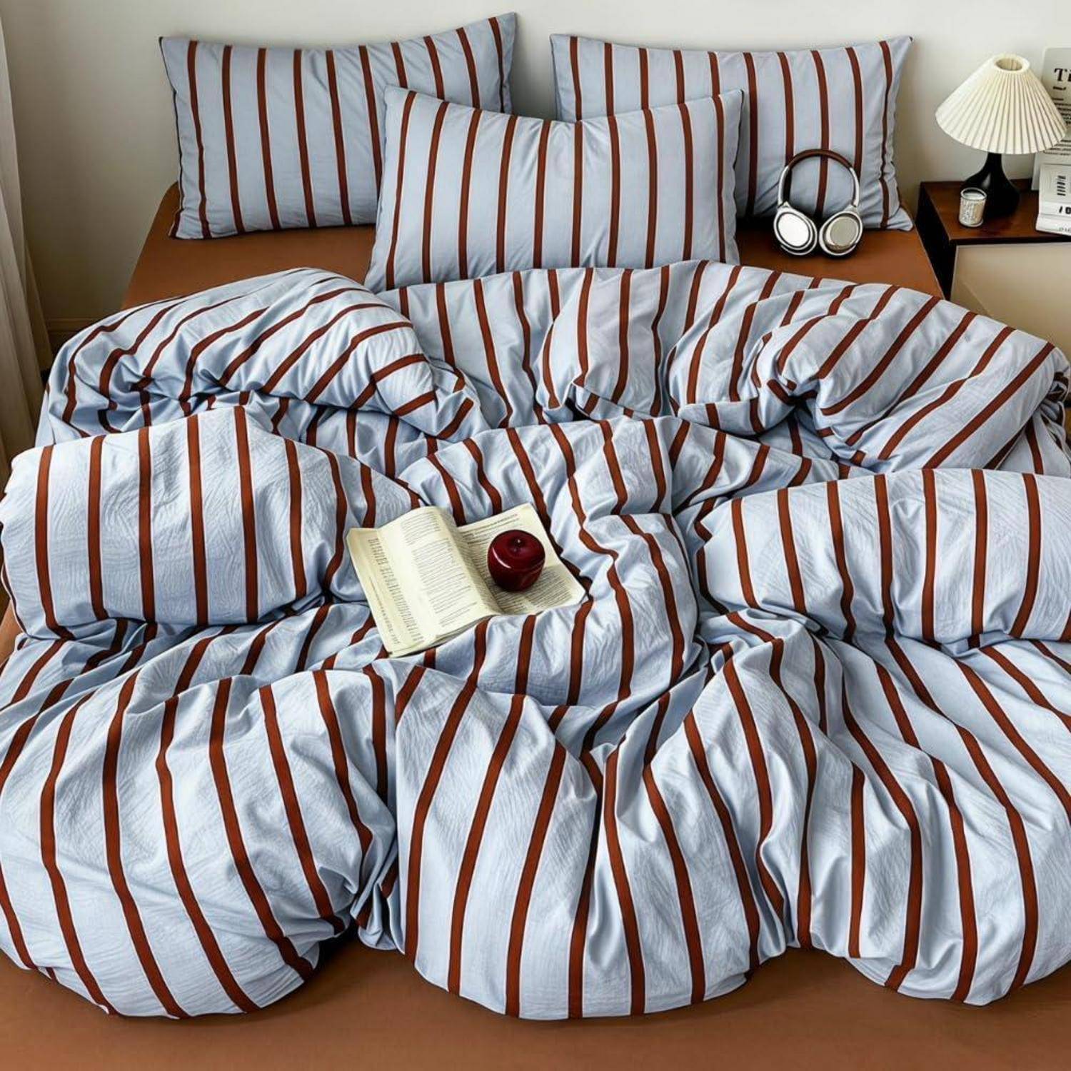 Ein ungemachtes Bett mit blau-weiß gestreifter Bettwäsche, Kissen, einem offenen Buch und einer Kerze obenauf.