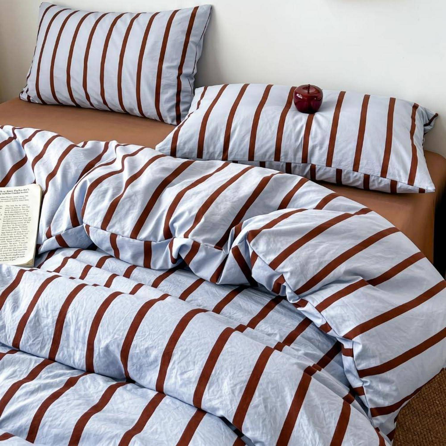 Gestreiftes Bettwäsche-Set auf einem Bett, mit passenden Kissenbezügen und einer Bettdecke in weiß-braunen Streifen.