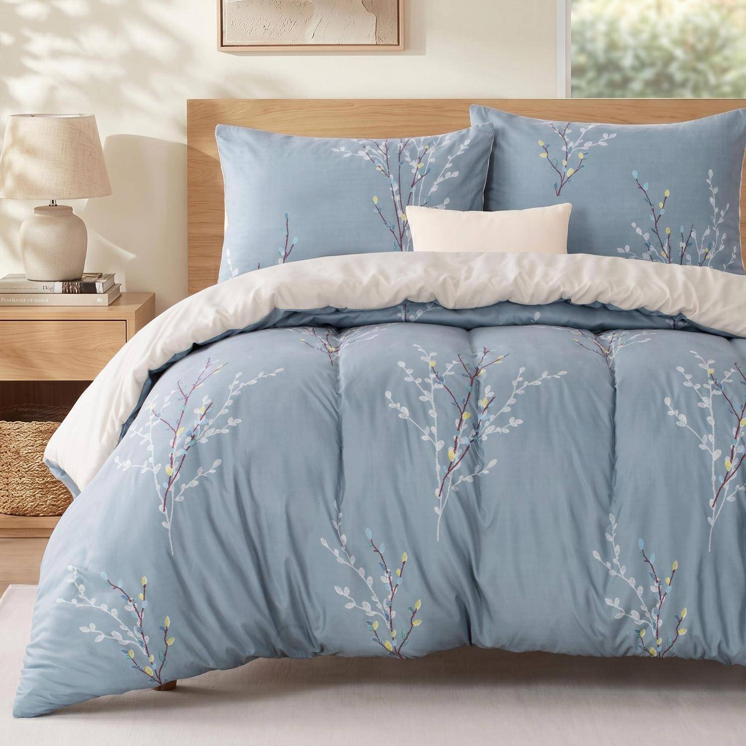 Ein ordentlich gemachtes Bett mit blauer Blumenbettwäsche und Kissen, eine weiße Decke und ein Nachttisch mit Lampe in einem weichen, minimalistischen Schlafzimmer.