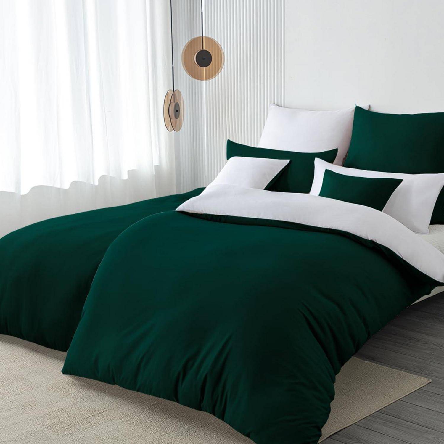 Ordentlich gemachtes Bett mit dunkelgrüner Bettwäsche und weißen Kissen in einem hellen, minimalistischen Schlafzimmer neben einem Fenster und hängender Wanddekoration.