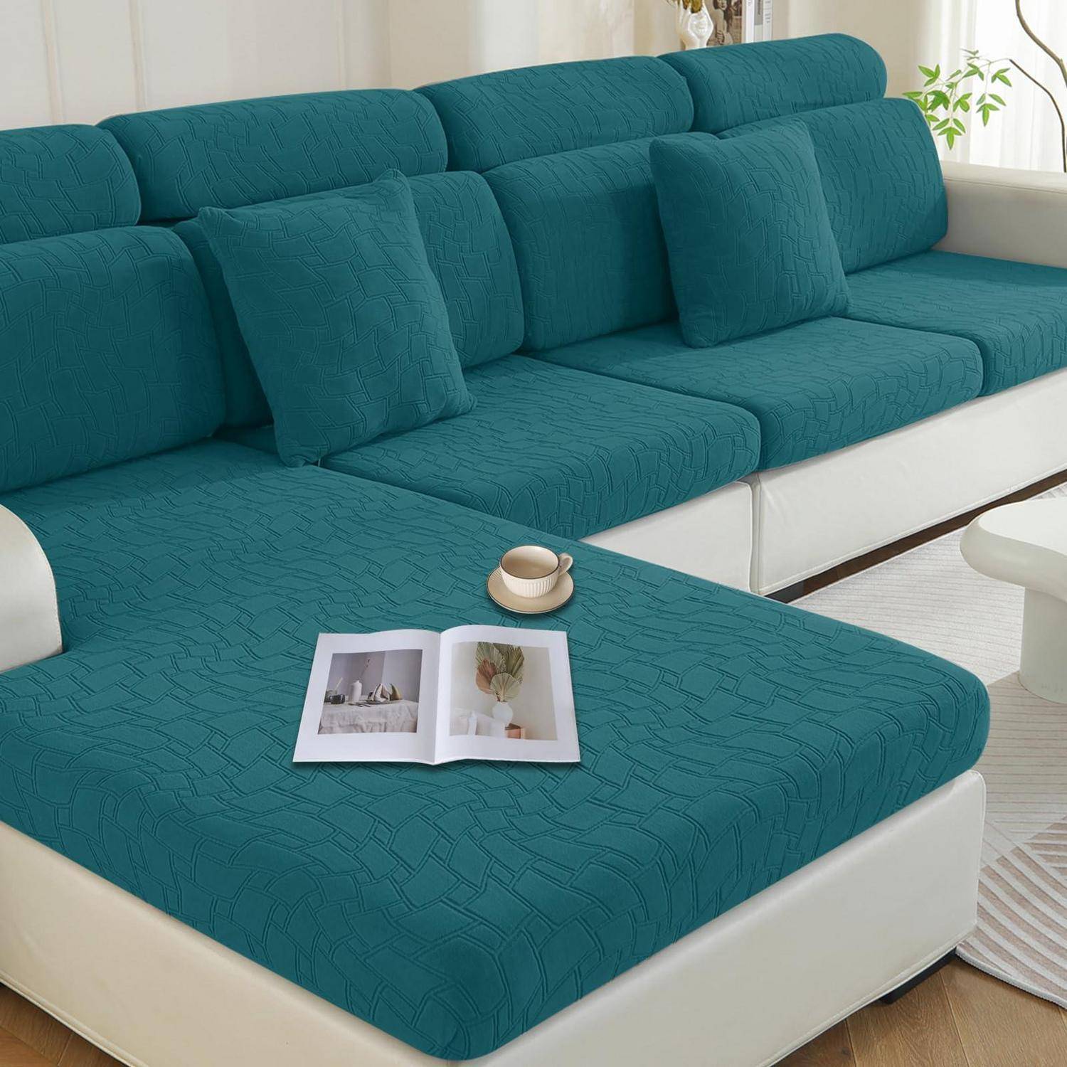 Tealblaues Ecksofa mit weißem Untergestell in einem hellen Wohnzimmer, mit einer aufgeschlagenen Zeitschrift und einer Tasse auf der Chaiselongue.