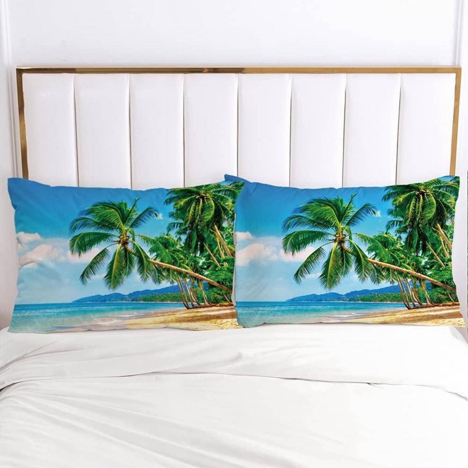 Bett mit zwei tropischen Strandmotiv-Kissen vor einem weißen gesteppten Kopfteil und weißer Bettwäsche.