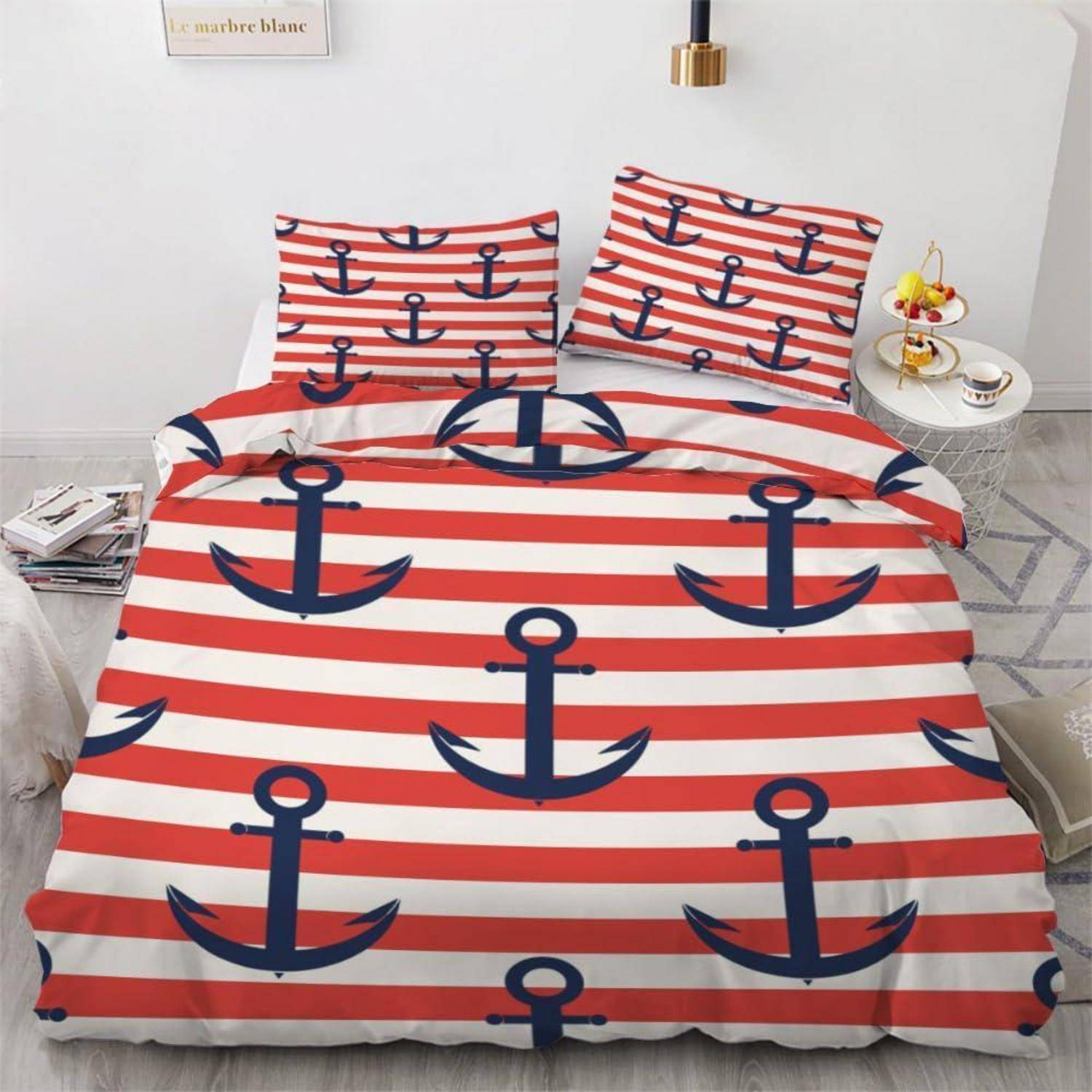 Ein Bett mit rot-weiß gestreifter Bettwäsche mit marineblauen Ankermotiven, einschließlich passender Kissen, in einem hellen Schlafzimmer.