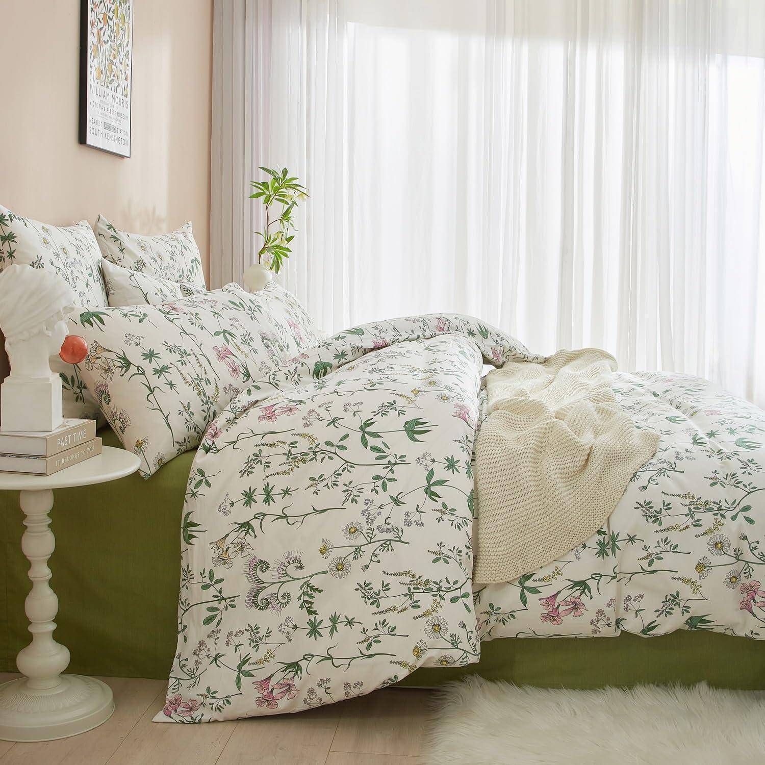 Helles Schlafzimmer mit einem Bett, das in weiße Blumenbettwäsche und grüner Basis gekleidet ist, neben einem kleinen weißen Nachttisch und transparenten Vorhängen.