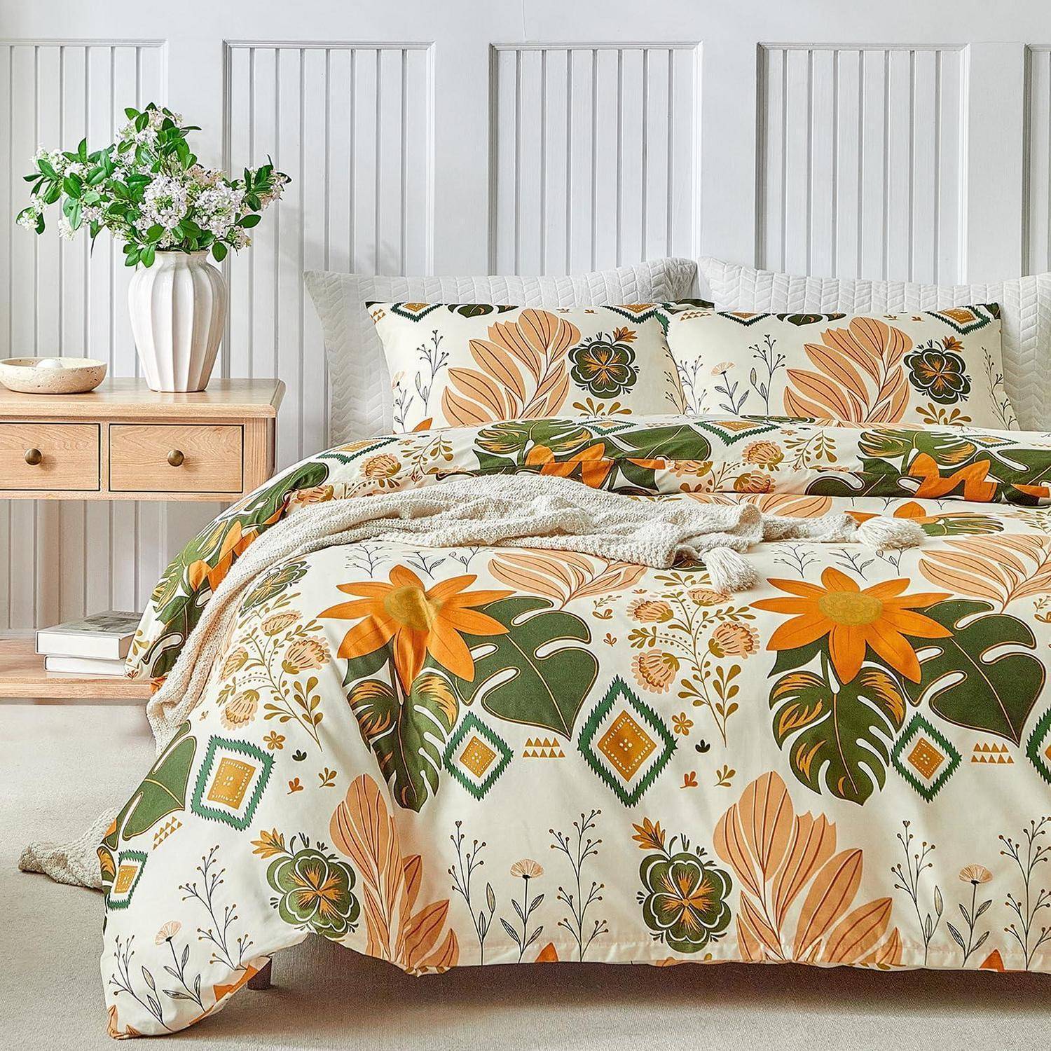 Steppdecke mit Blumenmuster und Kissen auf einem Bett in einem hellen Schlafzimmer mit weißer Vertäfelung, Nachtschrank aus Holz und Blumenvase.