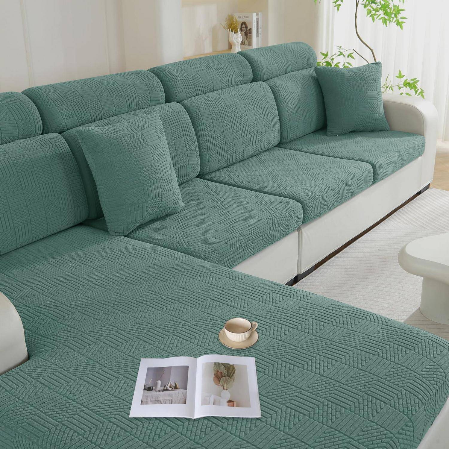 Ein türkisfarbenes Ecksofa mit passenden Kissen und ein aufgeschlagenes Magazin auf der Chaiselongue neben einer kleinen Tasse in einem hellen Wohnzimmer.