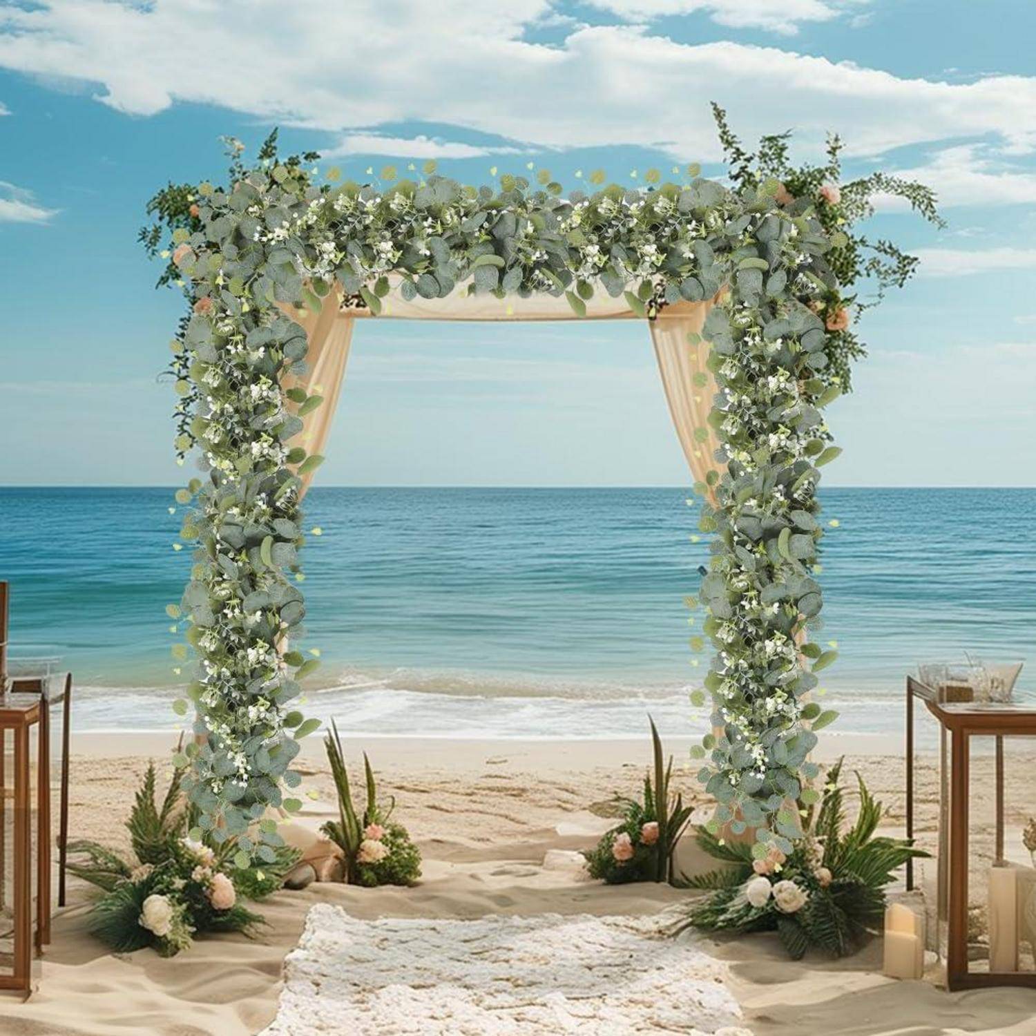 Hochzeitsbogen am Strand, dekoriert mit Grünpflanzen und weißen Blumen auf sandigem Untergrund, mit Meer und Himmel im Hintergrund.