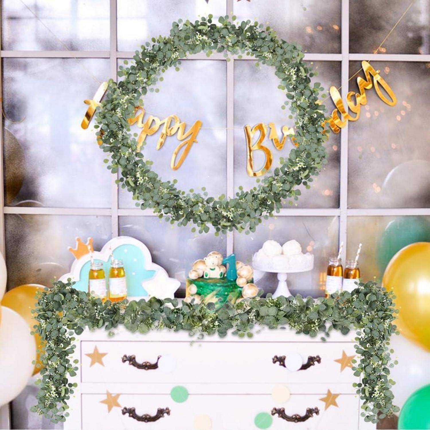 Geburtstagsfeier-Hintergrund mit einem großen Eukalyptus-Kranz, goldenen "Happy Birthday""-Buchstaben und einem dekorierten Nachtischtisch mit Ballons und Kuchen.