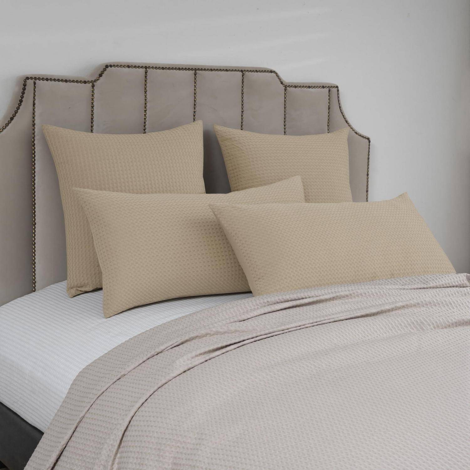 Ein ordentlich gemachtes Bett mit geknöpftem gepolstertem Kopfteil, beigefarbenen Kissen und einer leicht strukturierten Decke in einem neutralen Schlafzimmer.