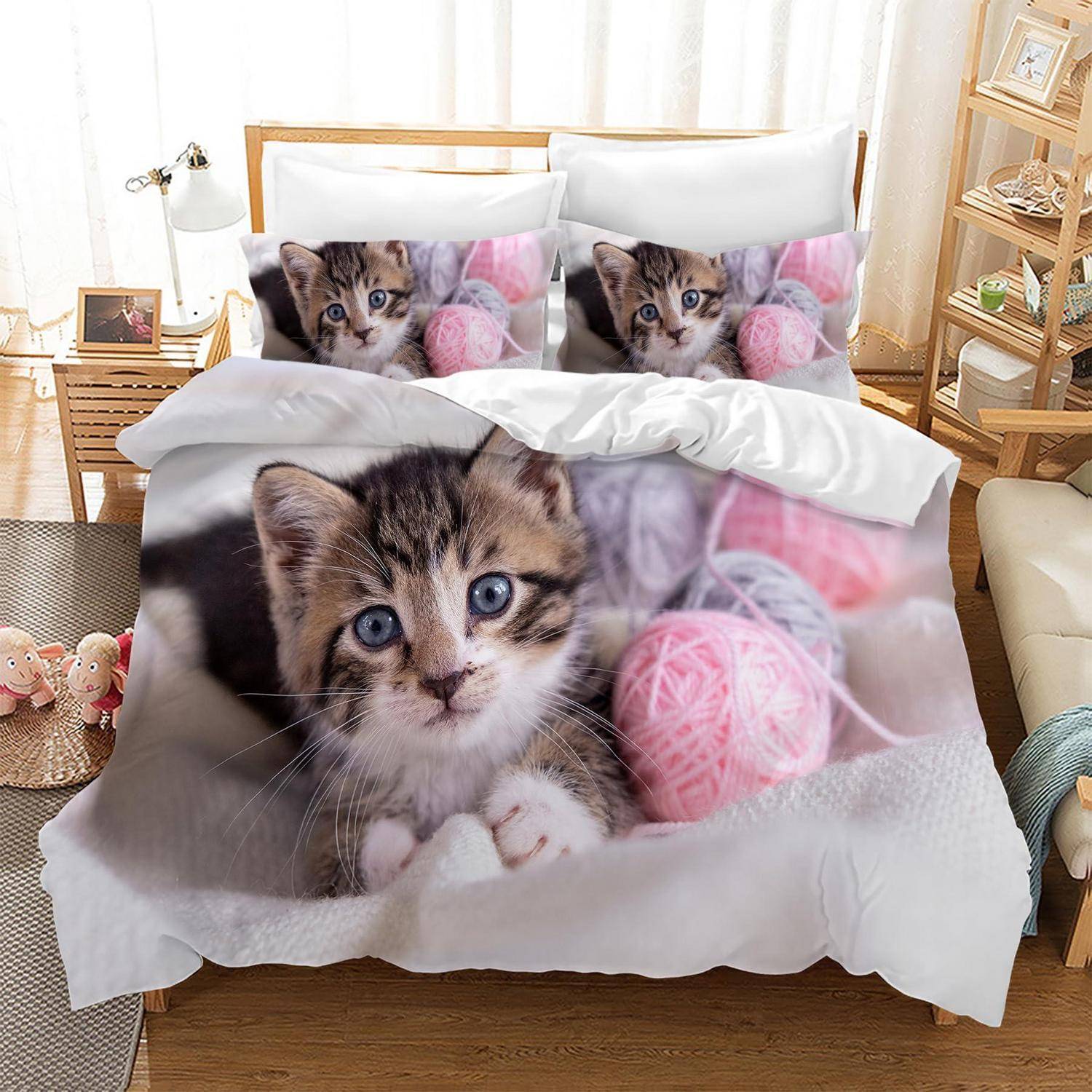 Bett mit katzenmuster-Bettwäsche und Kissen, mit einer Nahaufnahme eines getigerten Kätzchens und rosafarbenen Wollknäueln in einem hellen Schlafzimmer.