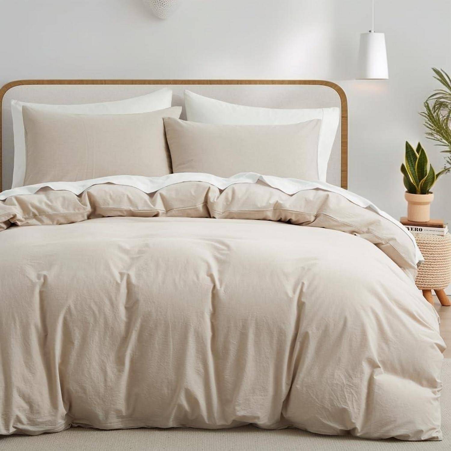 Minimales Schlafzimmer mit einem ordentlich gemachten Bett, beigefarbiger Bettwäsche und Kissen, einem hölzernen Kopfteil und einer kleinen Topfpflanze daneben.