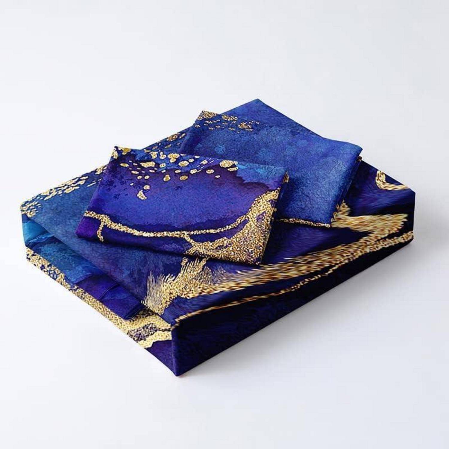 Stapel aus gefalteten blauem Stoff mit Goldmuster und Blumen- sowie Rankenmotiven auf weißem Hintergrund.