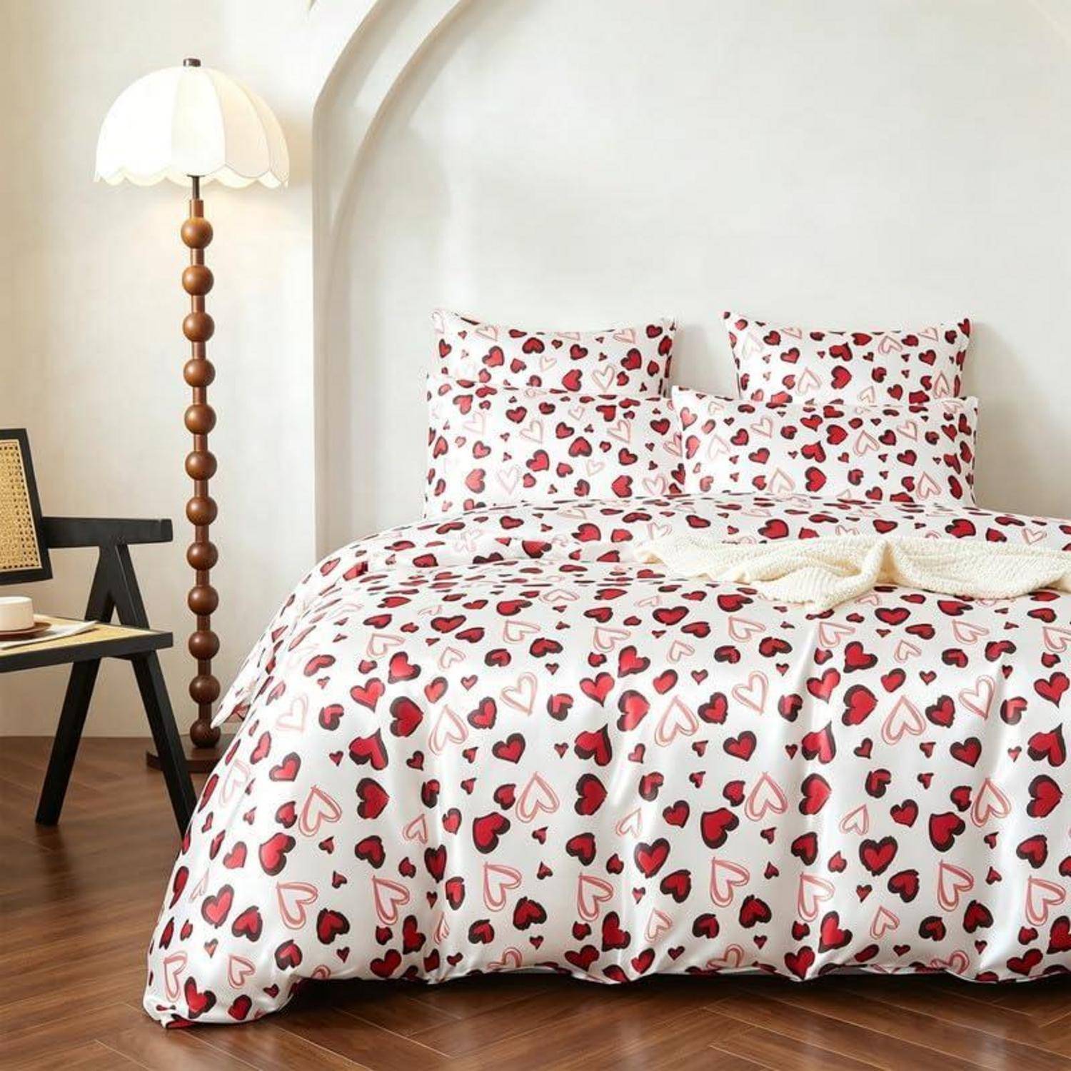 Bett mit herzgemusterter Bettwäsche in einem hellen Schlafzimmer, neben einer Stehleuchte und einem kleinen Nachttisch.