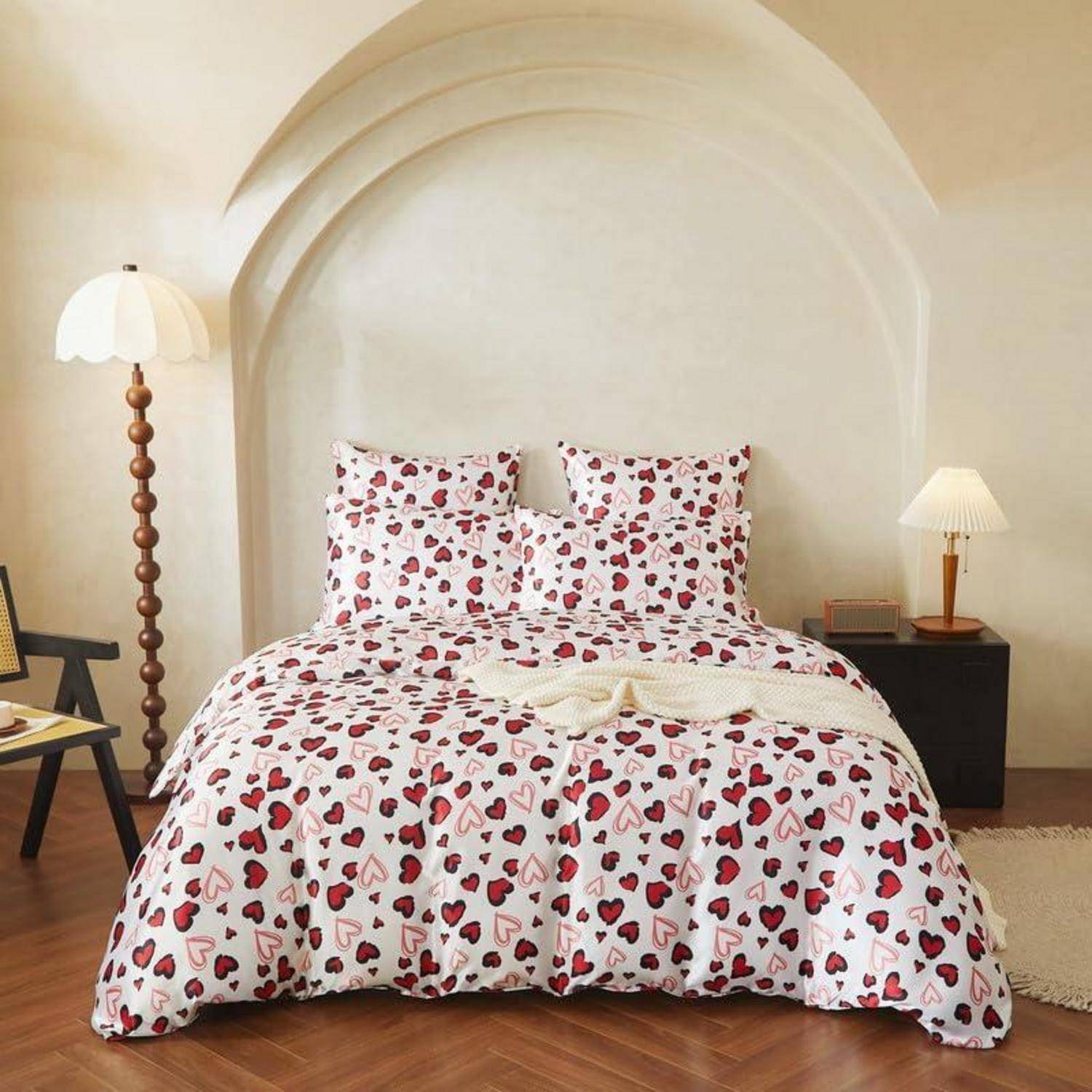 Ein ordentlich gemachtes Bett mit herzförmig gemusterter Bettwäsche und Kissen befindet sich in einem minimalistischen Schlafzimmer mit gewölbtem Wanddetail und zwei Nachttischlampen.