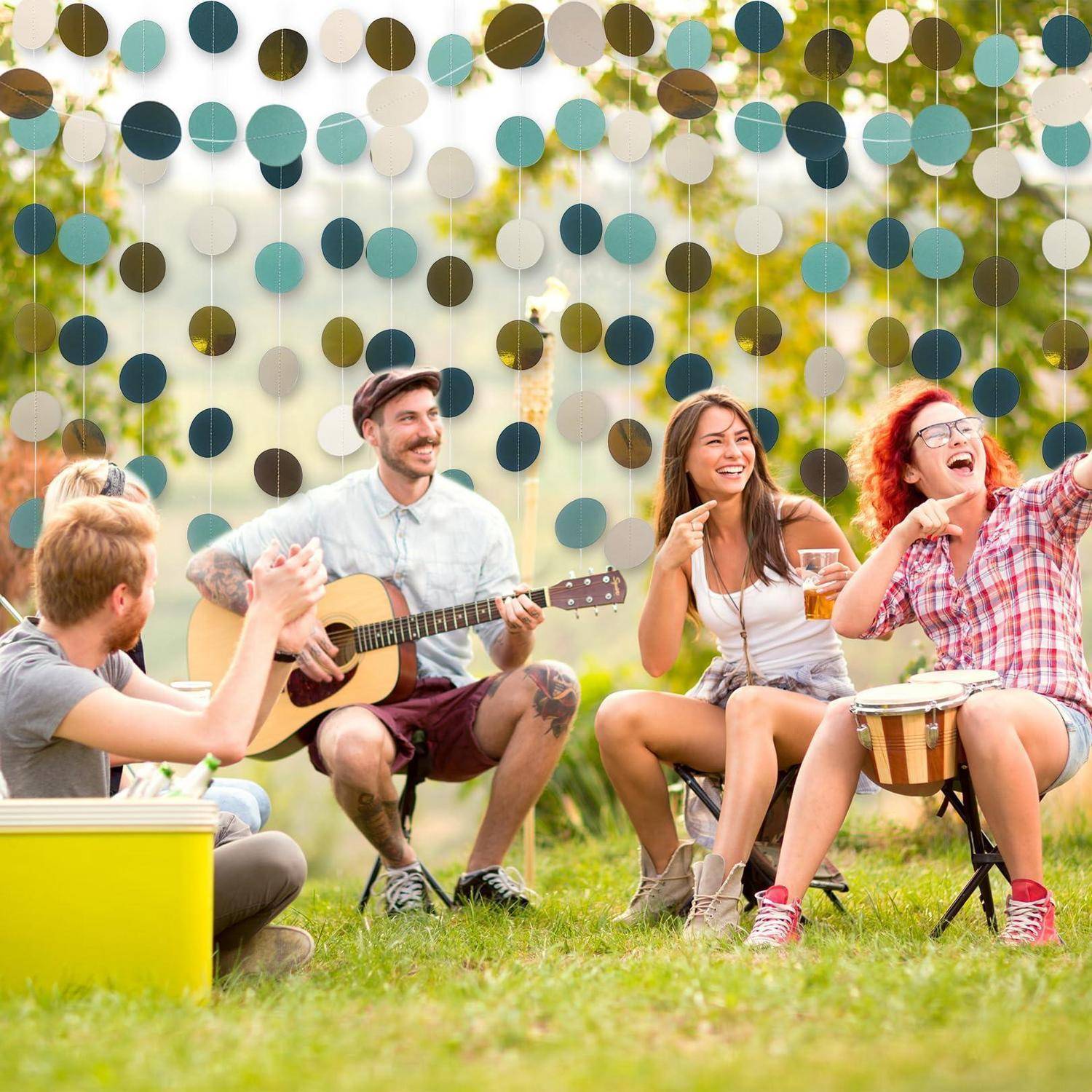 Freunde sitzen draußen, machen Musik und klatschen bei einer lockeren Gartenfete mit hängenden Papierdekoration.