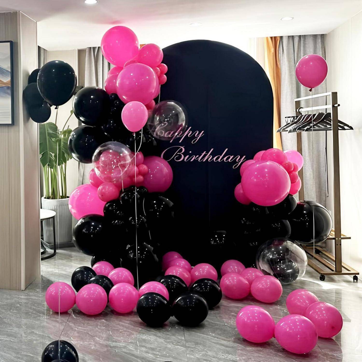 Rosa und schwarze Geburtstagsballondekoration um einen runden schwarzen Hintergrund mit „Happy Birthday"-Text in einem dekorierten Zimmer.
