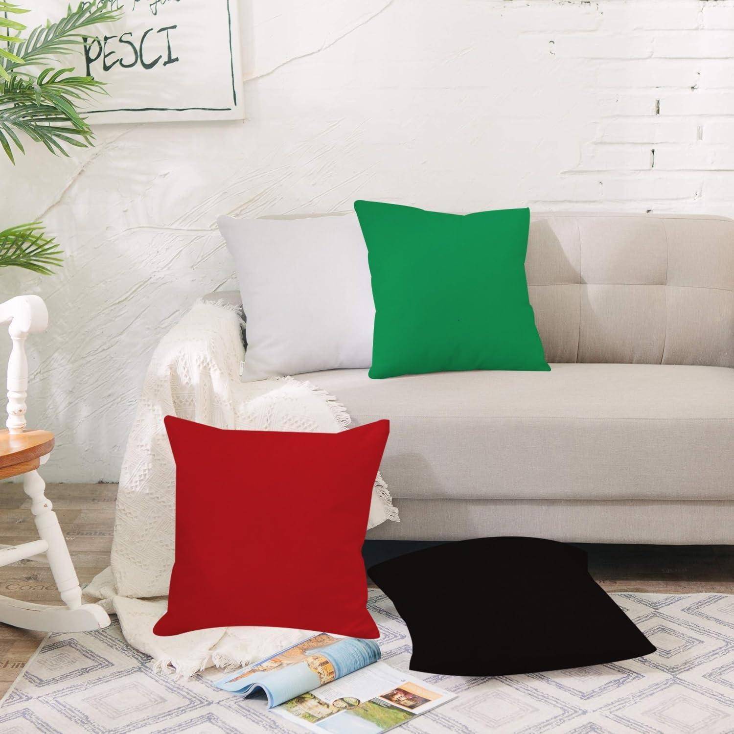 Ein beiges Sofa in einem hellen Wohnzimmer mit vier einfarbigen Dekokissen: weiß, grün, rot und schwarz, mit einer Zeitschrift auf dem Boden.