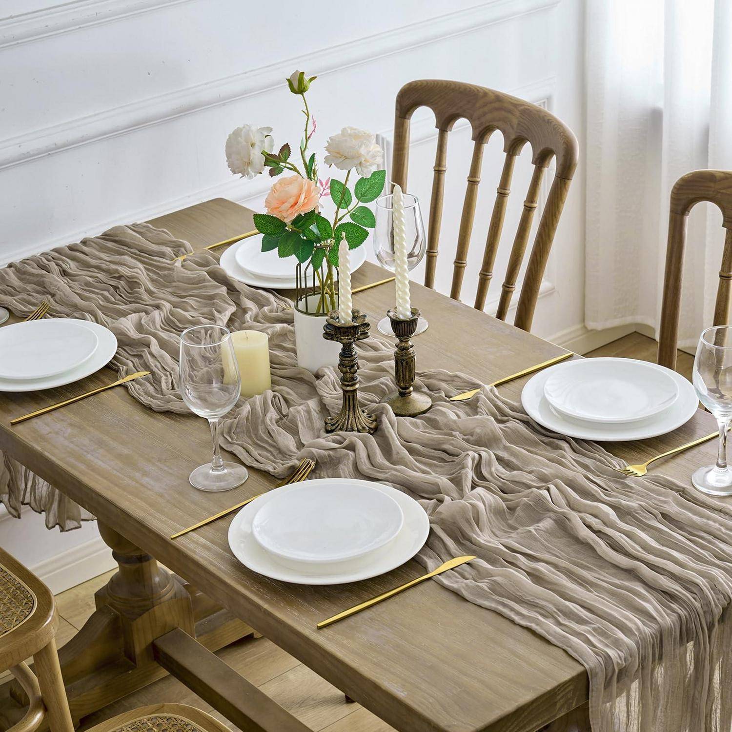 Stilvolles Esstischset für ein formelles Essen, mit weißen Tellern, Weingläsern, goldenem Besteck, Kerzenleuchtern und einer Blumenmitte auf einem drapierten Läufer.