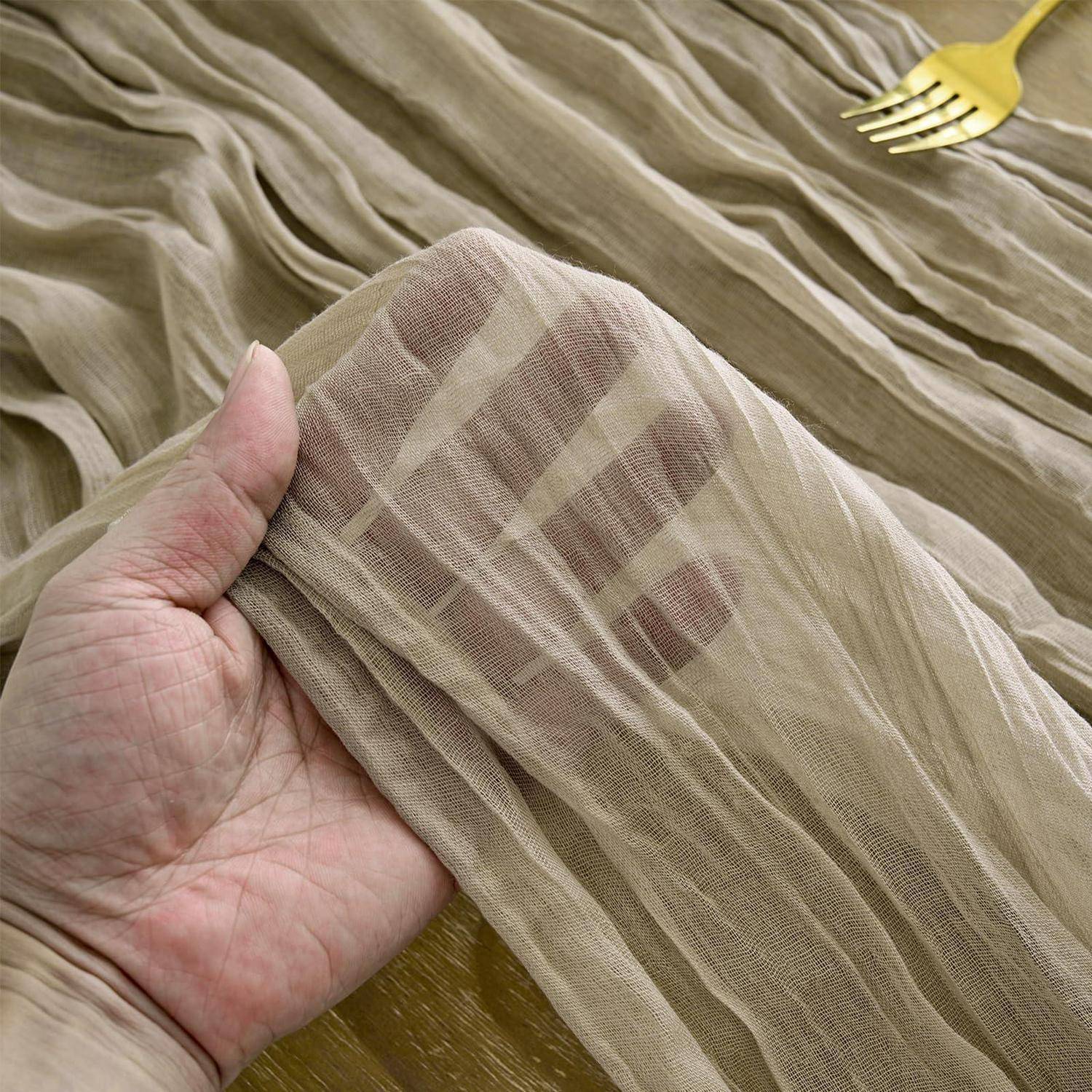 Hand, die ein durchsichtiges beiges gerafftes Stoffmuster hält, das seine leichte Textur und den Drape auf einem passenden Stoffhintergrund zeigt.