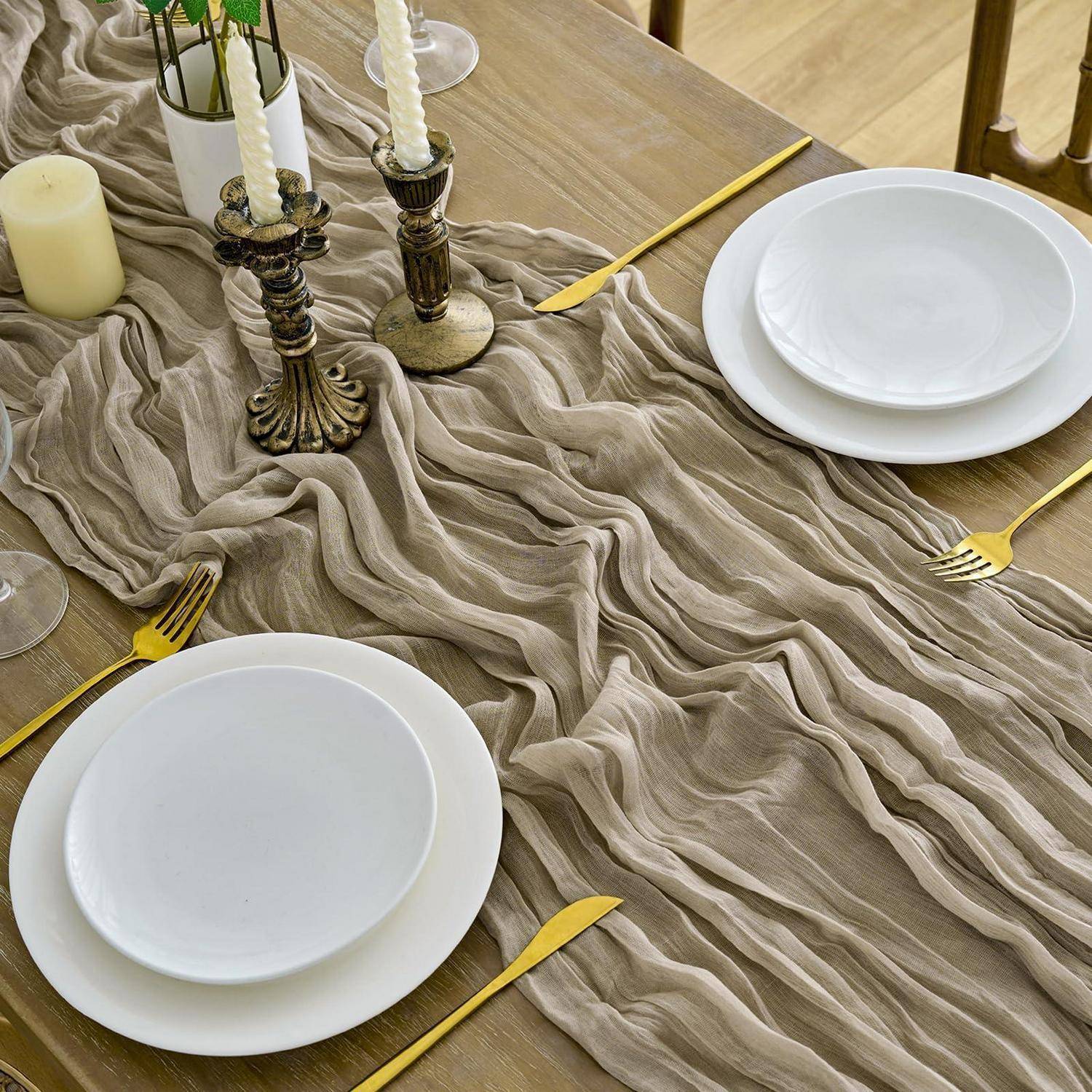Elegante Tischeindeckung mit weißen Tellern, goldenem Besteck, Kerzenleuchtern und einem strukturierten beigefarbenen Tischläufer auf einem Holztisch.