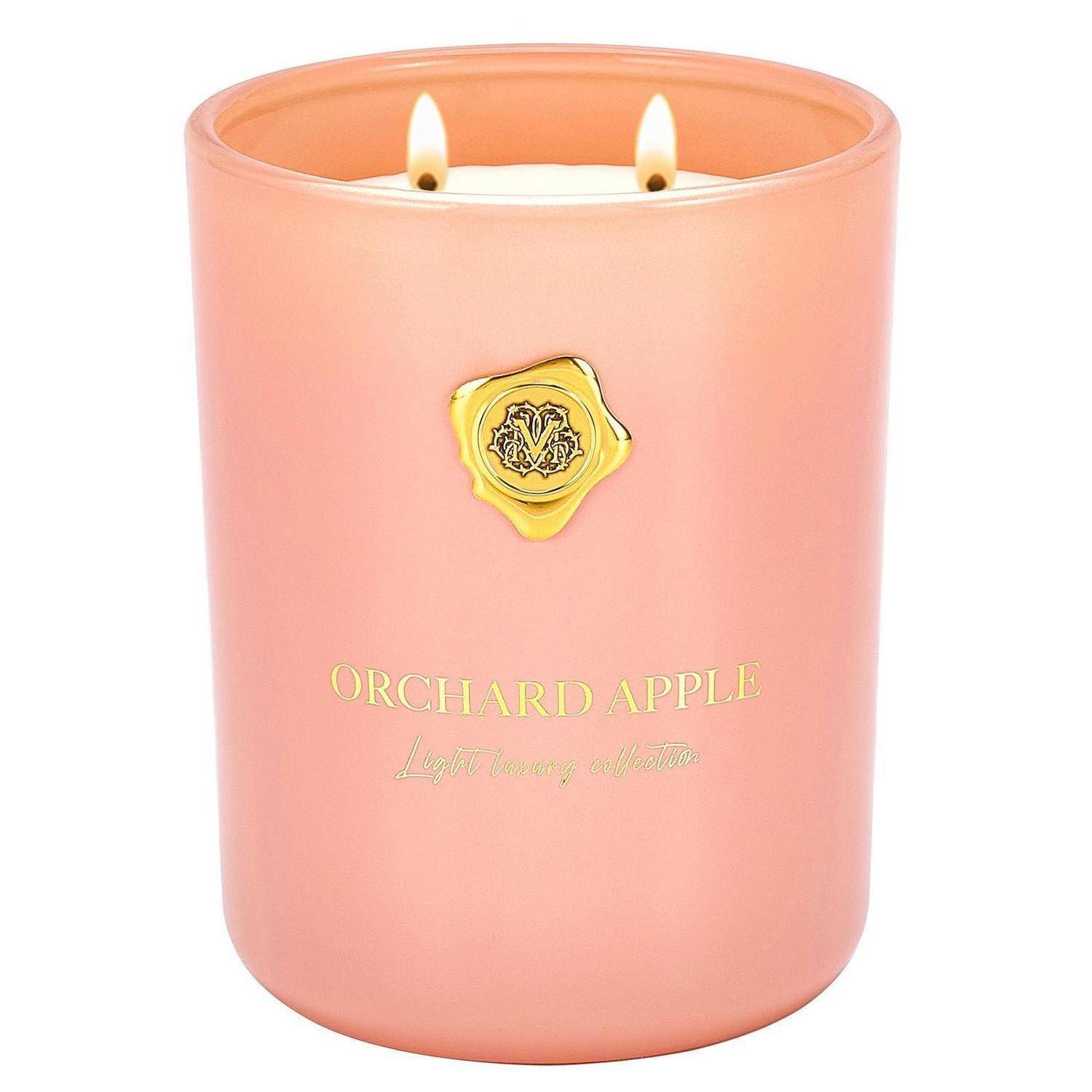 Duftkerze in Rosa in einem Glaskrug mit zwei brennenden Dochten und goldenem Etikett mit der Aufschrift „ORCHARD APPLE