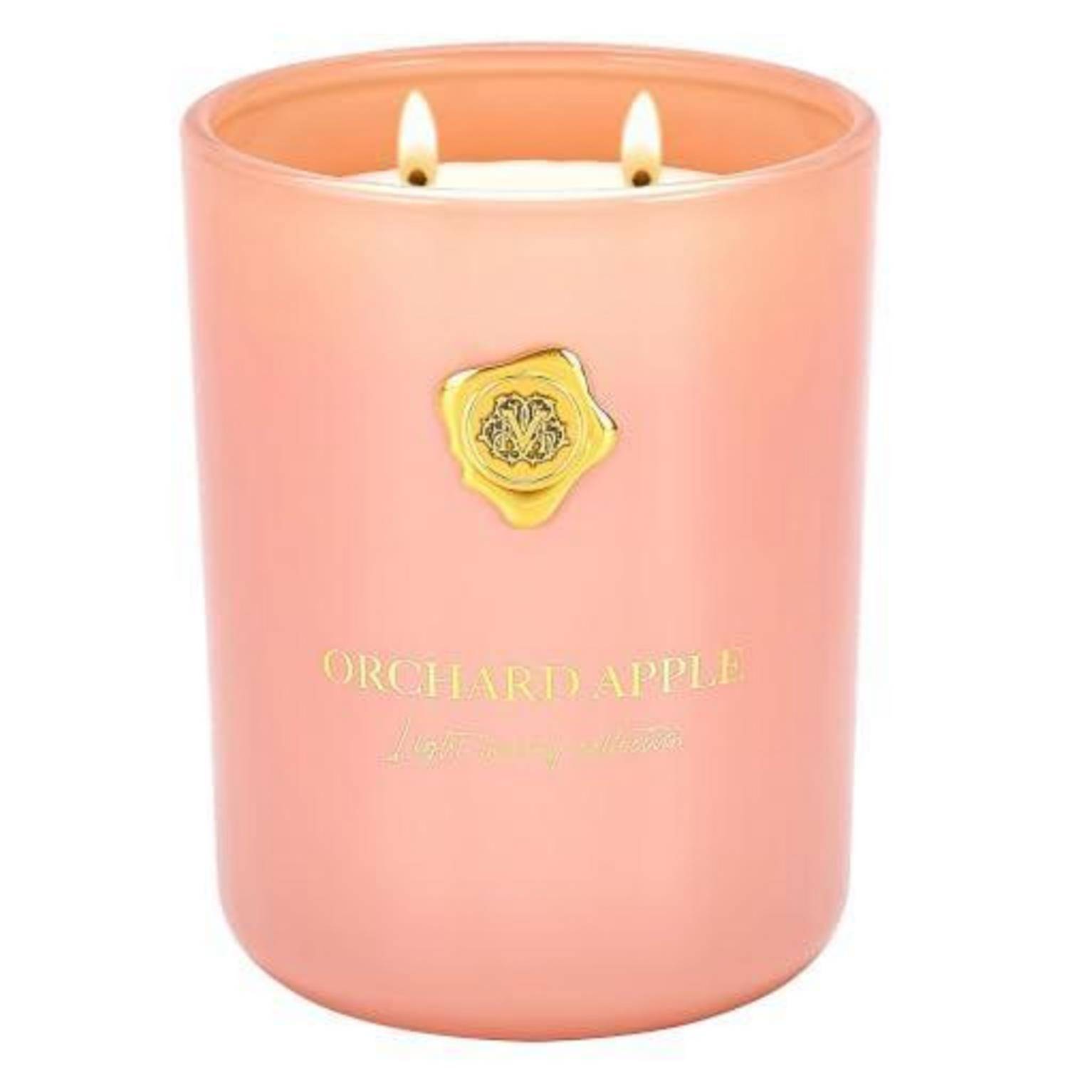 Rosa Kerzenglaskerze mit der Aufschrift "Orchard Apple"" mit zwei brennenden Dochten und einem goldenen Emblem auf der Vorderseite.