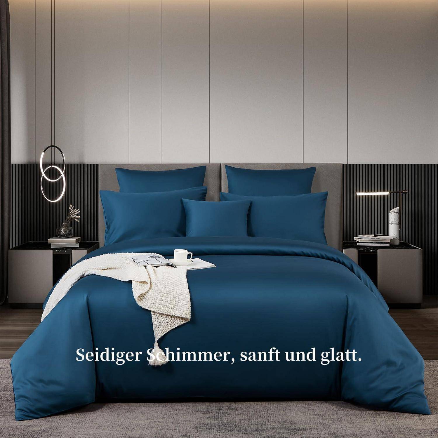 Stilvolles modernes Schlafzimmer mit einem blauen Bett und Bettwäsche, beleuchteten Nachttischen und dem deutschen Text „Seidiger Schimmer, sanft und glatt."