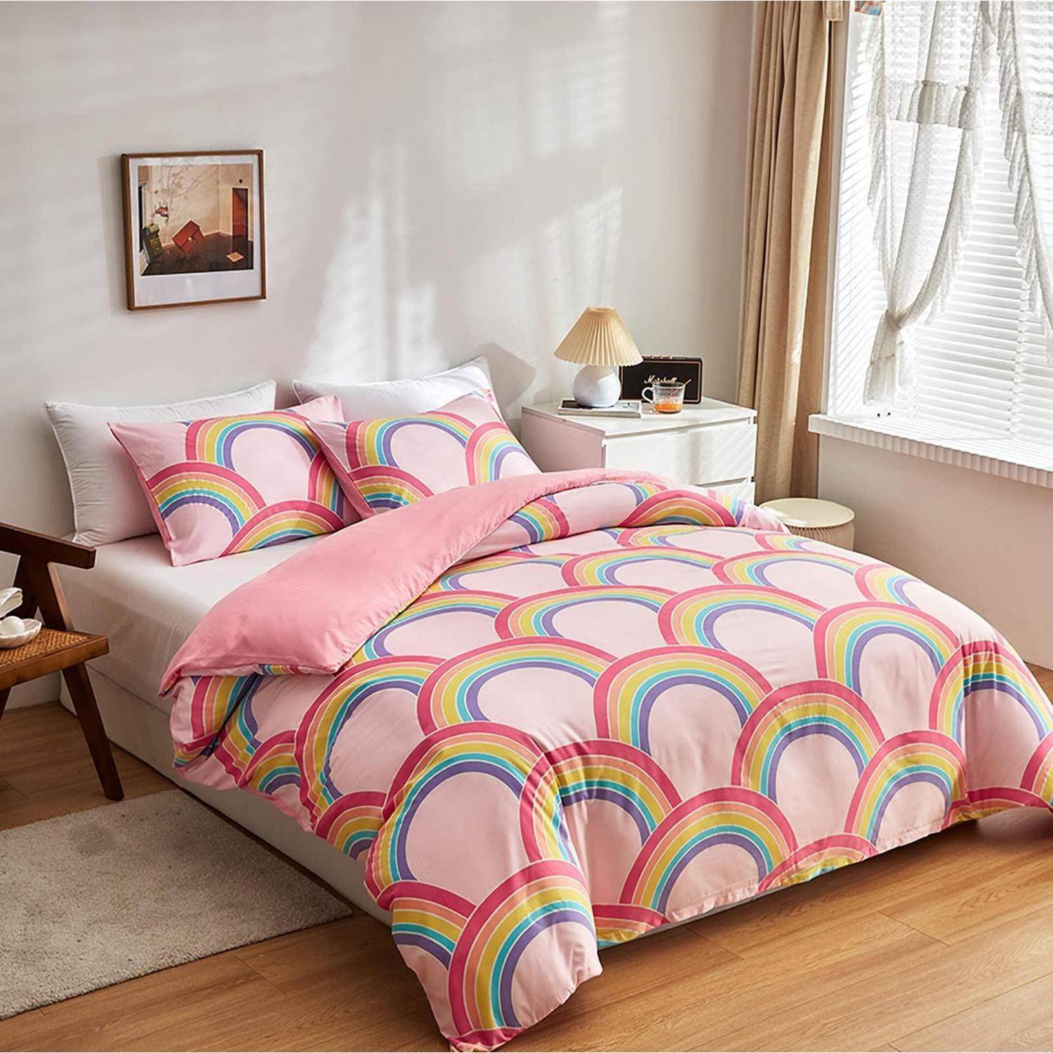Ein ordentlich gemachtes Bett mit rosa Regenbogenmuster-Bettwäsche und Kissen in einem hellen Schlafzimmer neben einem Fenster und einem Nachttisch.