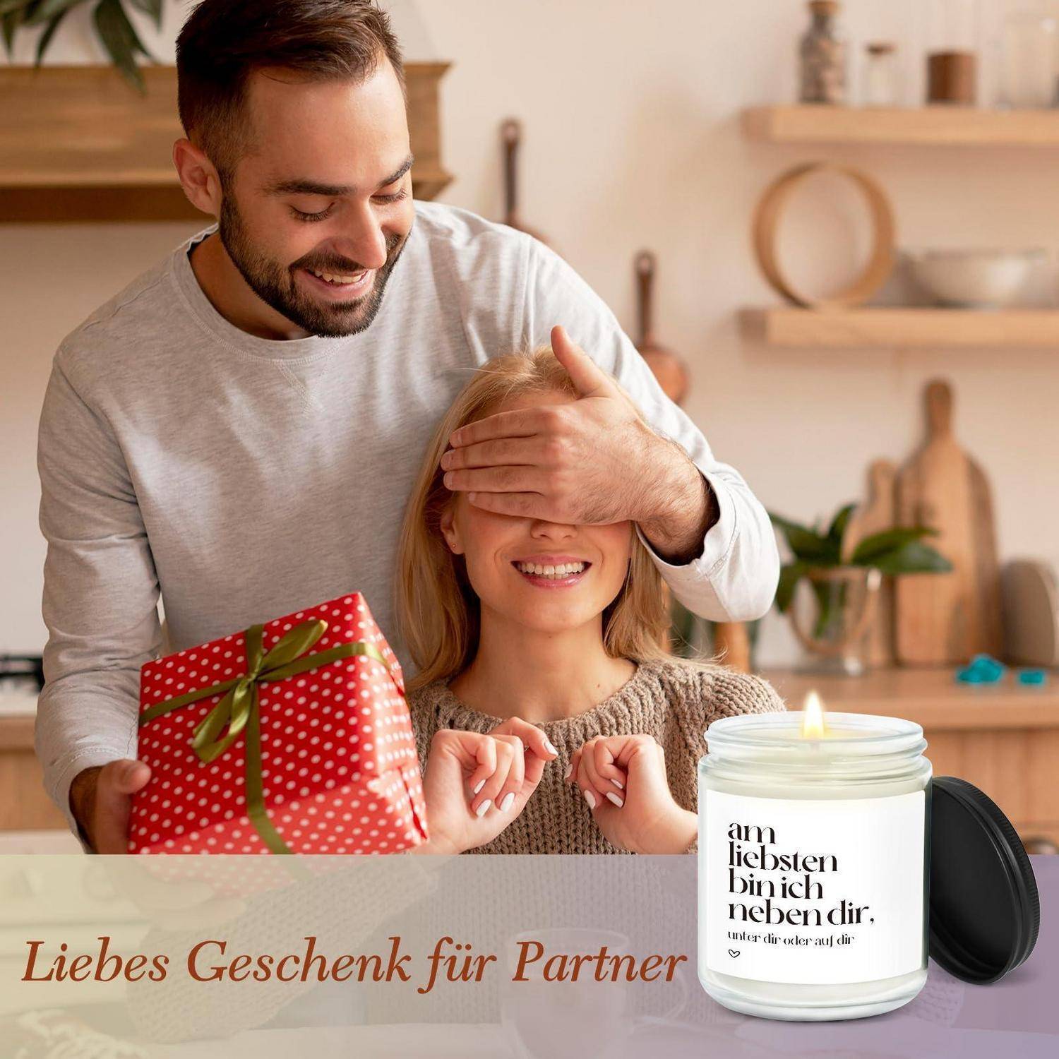 Ein Mann überrascht eine verbundene Frau mit einer roten Geschenkbox und einer brennenden Kerze mit der Aufschrift „am liebsten bin ich neben dir"; der Text sagt „Liebes Geschenk für Partner"".