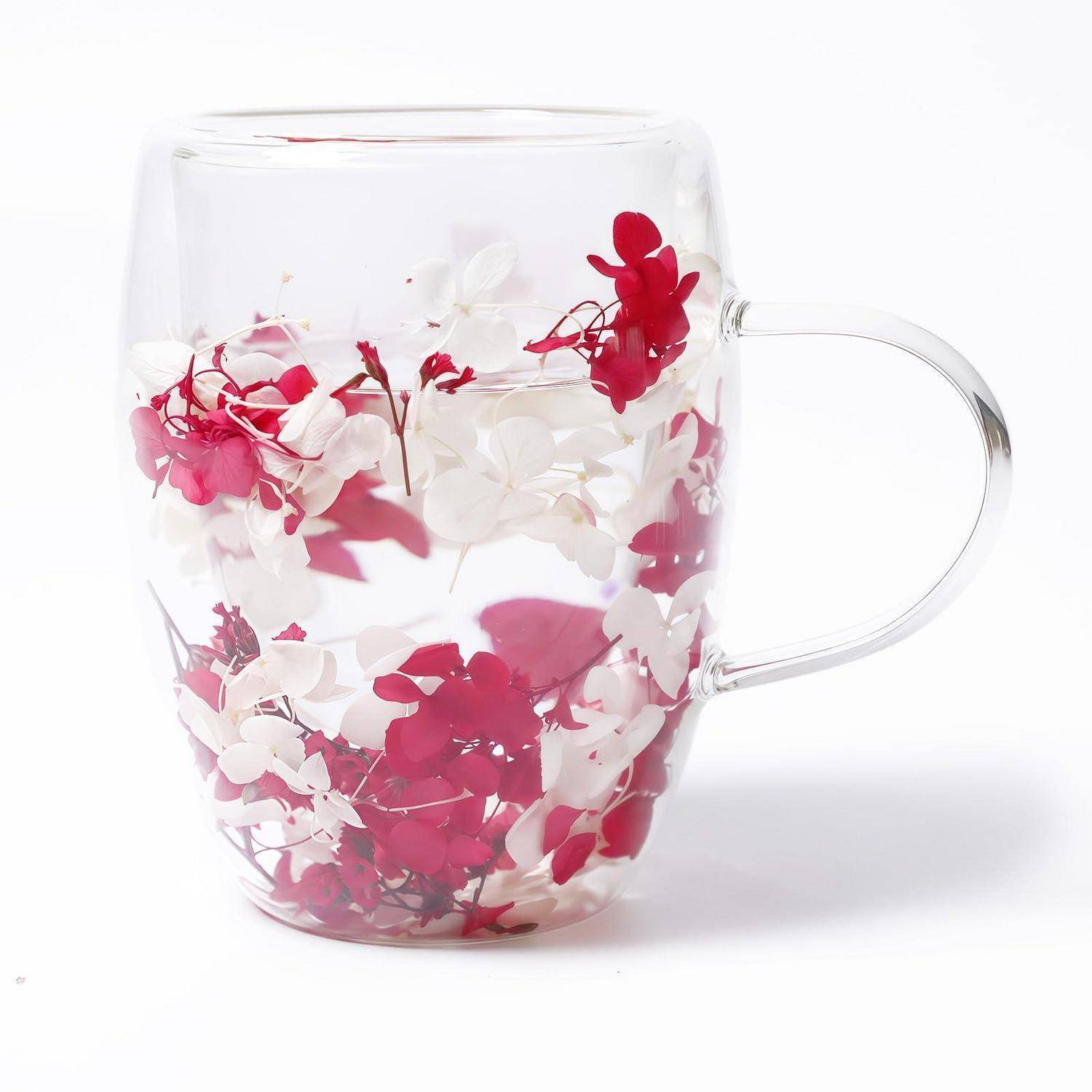 Klare Glastasse mit Henkel, innen dekoriert mit roten und weißen Blütenblättern auf weißem Hintergrund.