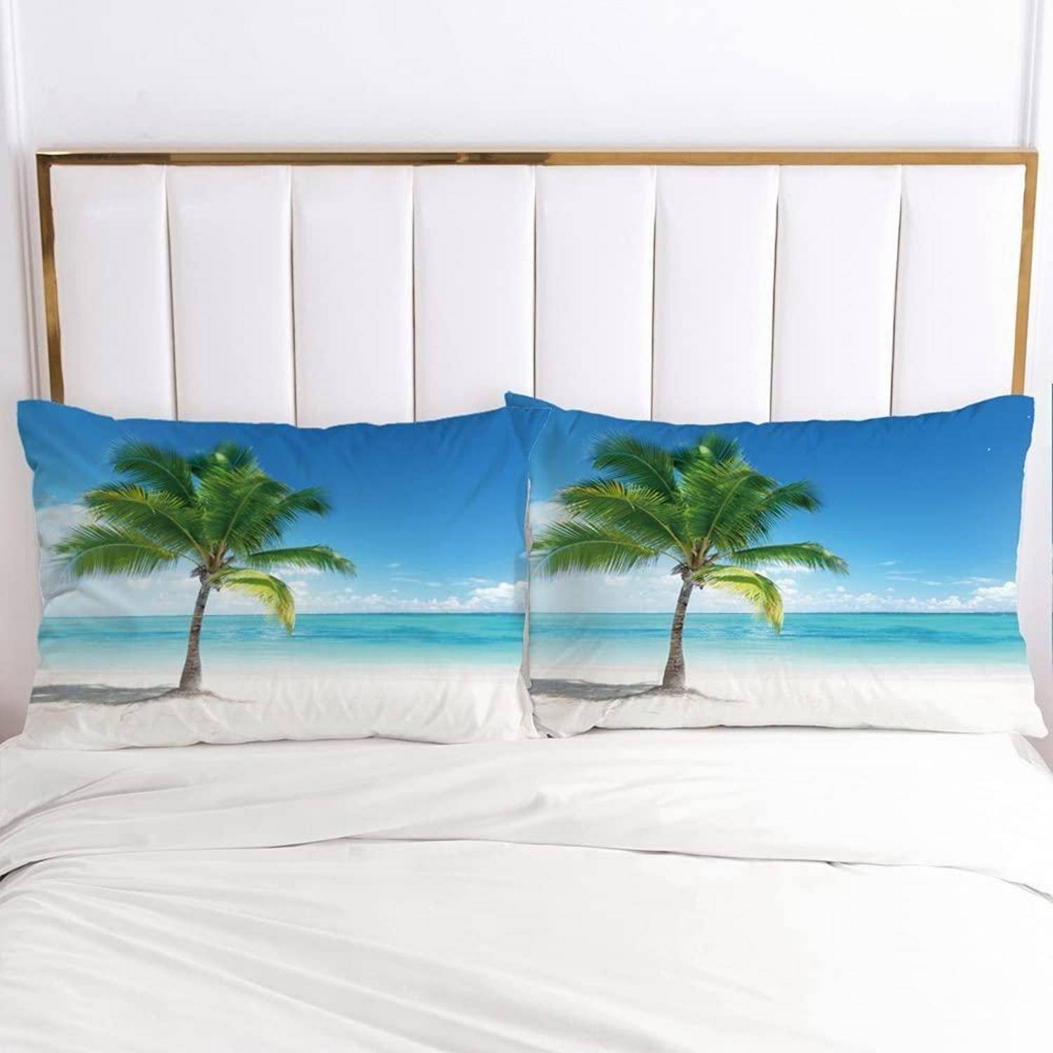 Ein Bett mit zwei Kissen mit Palmenbäumen und Strandszenen vor einem weißen Kopfteil, das ein tropisches, strandorientiertes Schlafzimmeraccessoires schafft.