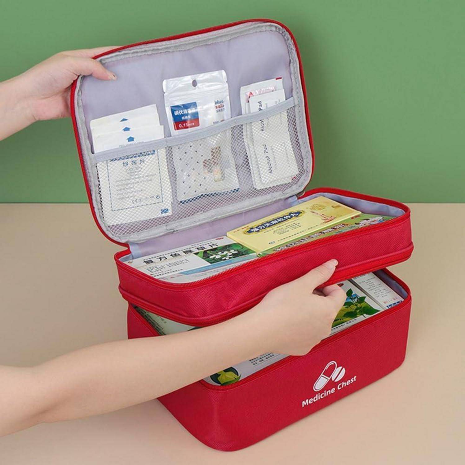 Hände ordnen einen roten Medizinschrank-Organizer mit zwei übereinander gestapelten Reißverschlussfällen, der gepackte Erste-Hilfe- und Medikamentenvorräte in Netztaschen zeigt.