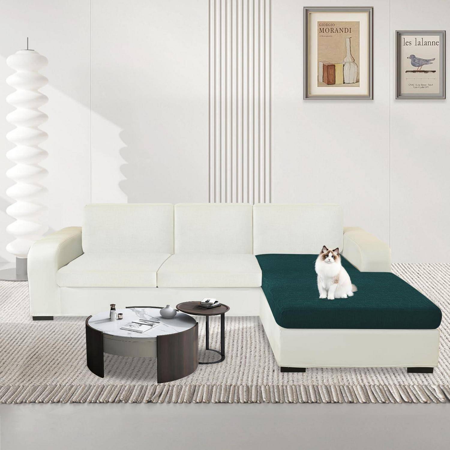 Modernes weißes Wohnzimmer mit einem Ecksofa, rundem Couchtisch, gerahmter Wandkunst, einer Stehleuchte und einer Katze, die auf einem dunkelgrünen Chaiselongue-Sitz sitzt.