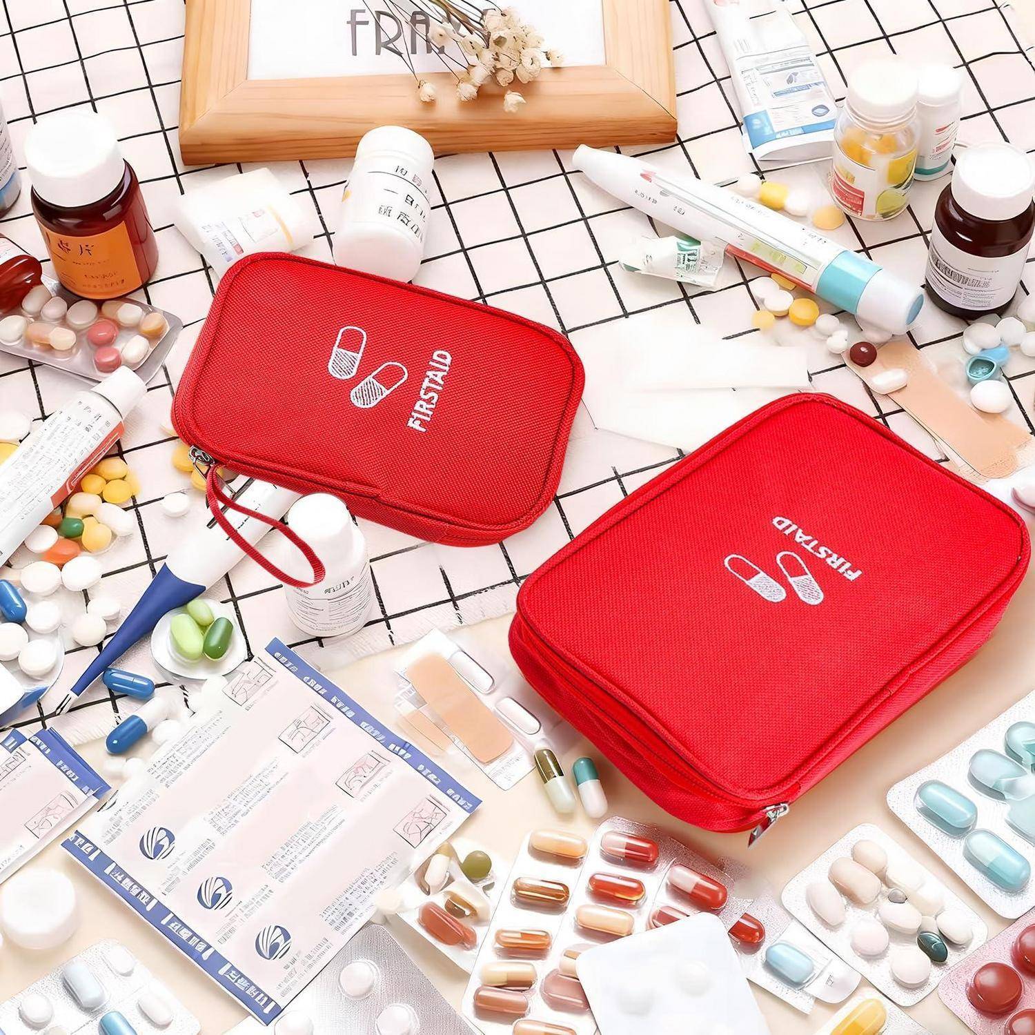 Zwei rote Erste-Hilfe-Kästen, umgeben von verschiedenen Tabletten, Salben und medizinischen Materialien auf einer karierten Oberfläche.