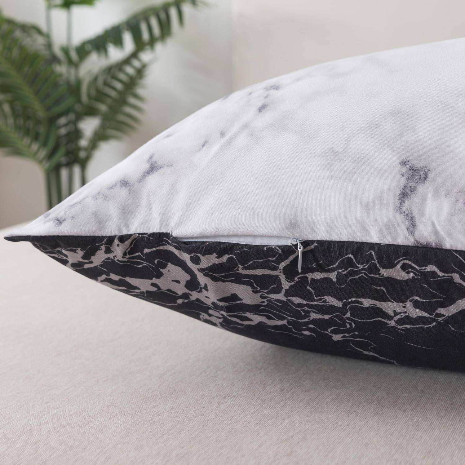 Dekorativer Wurf-Kissenbezug mit Marmormuster mit weißer Oberseite und schwarzem Sockel auf einem hellen Sofa, mit unscharfer Pflanze im Hintergrund.