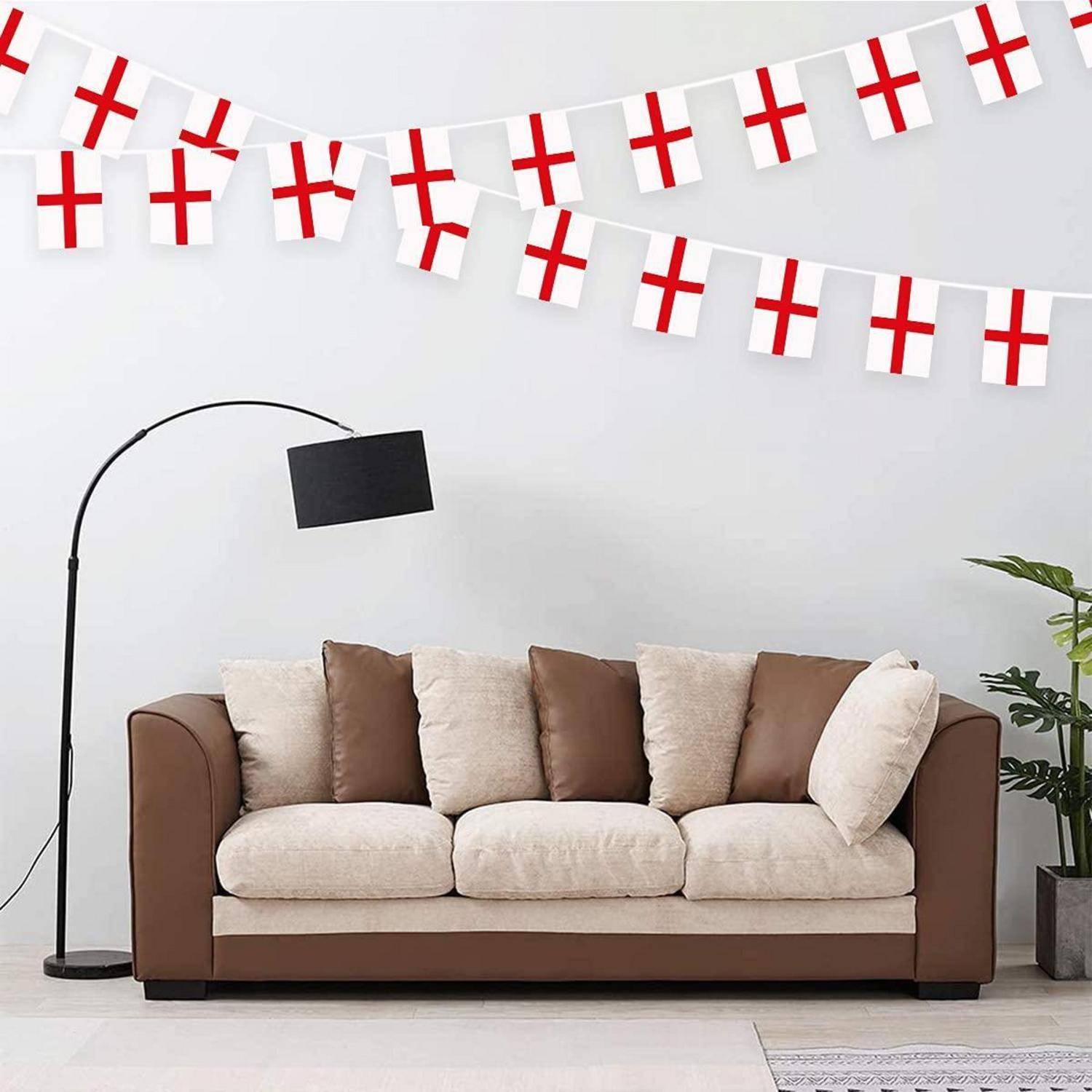 Wohnzimmer mit einem braun-cremefarbenen Sofa unter Girlanden mit St.-George's-Cross-Flaggen, was auf England-themed Dekoration hindeutet.