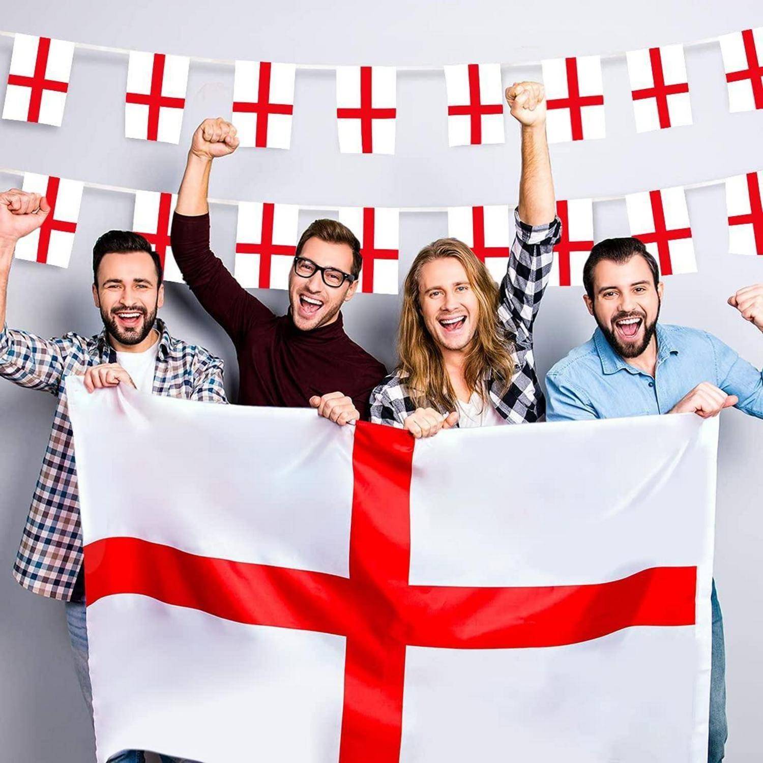 Vier jubelnde Fans halten eine England-Flagge, hinter ihnen ist Wimpelkette mit dem Georgskreuz.