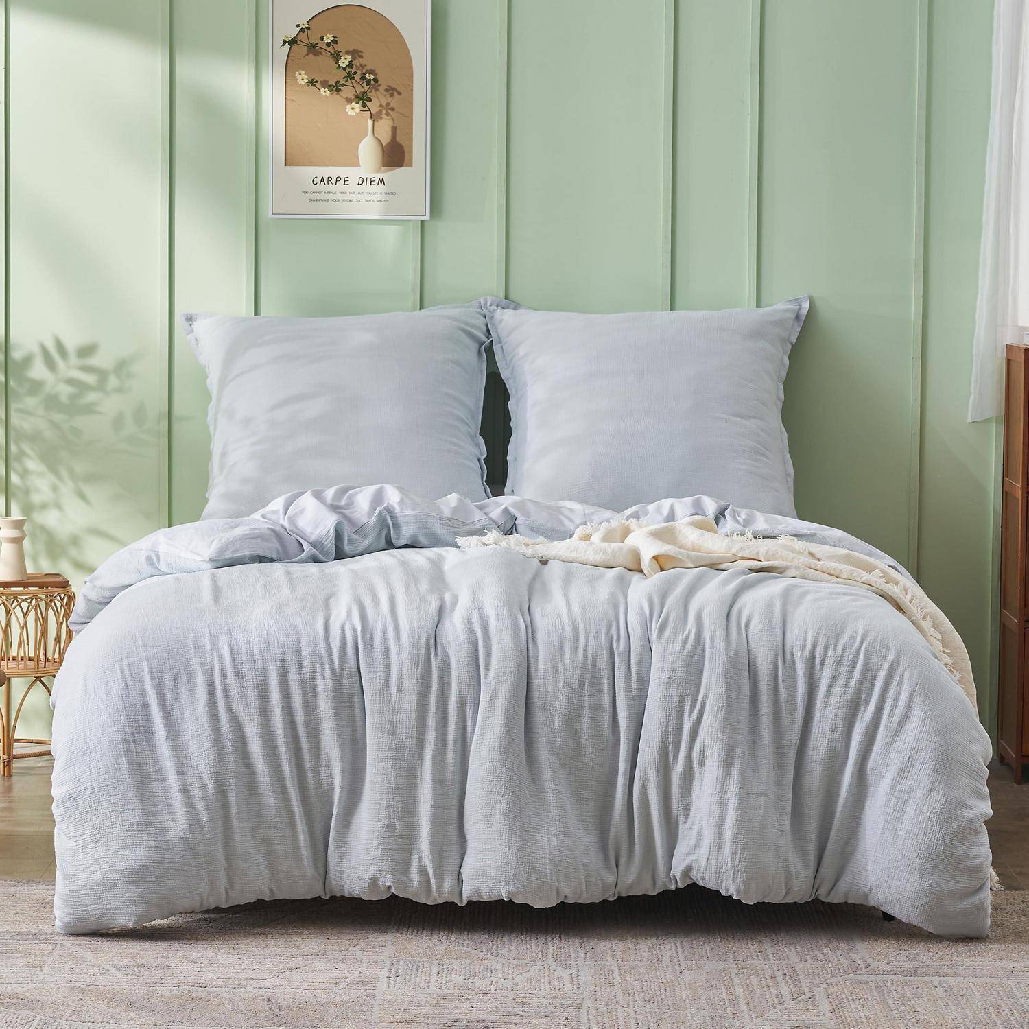 Ein ordentlich gemachtes Bett mit hellblauem Bettzeug und Kissen vor einer hellgrünen Holzpaneelwand mit einem „Carpe Diem