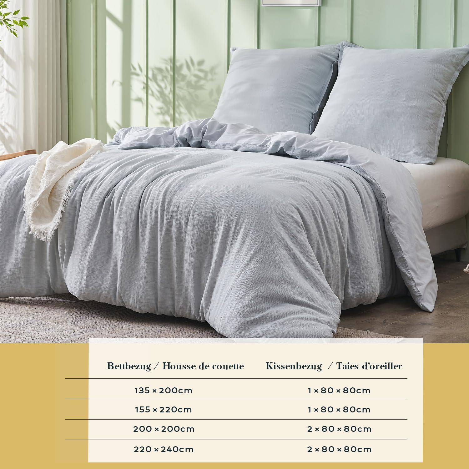 Graues Bettdecken-Set in einem Schlafzimmer gezeigt, mit einer Größentabelle darunter, die Bettwäsche- und Kissenbezugsgrößen auf Französisch und Deutsch auflistet.