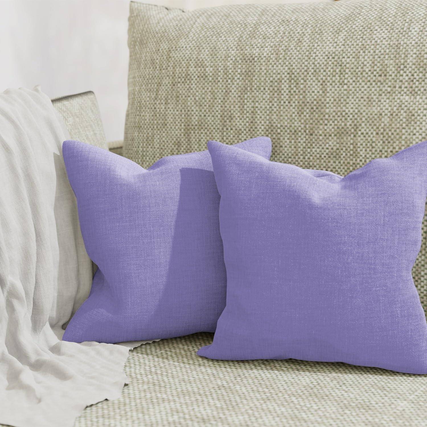 Zwei Lavendelkissen auf einem beige strukturierten Sofa neben einer weiß drapierte Decke.