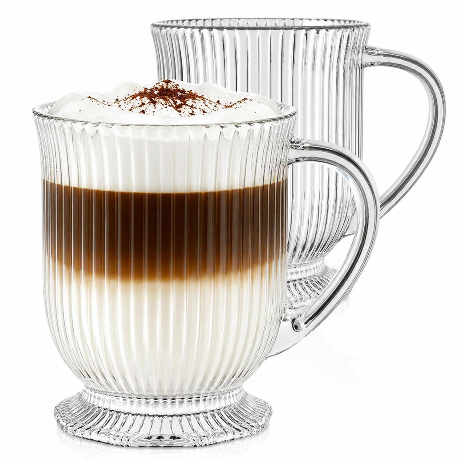 Zwei transparente gerillte Glastassen, eine gefüllt mit geschichtetem Kaffee, oben mit Schaum und Kakao, die andere leer dahinter.